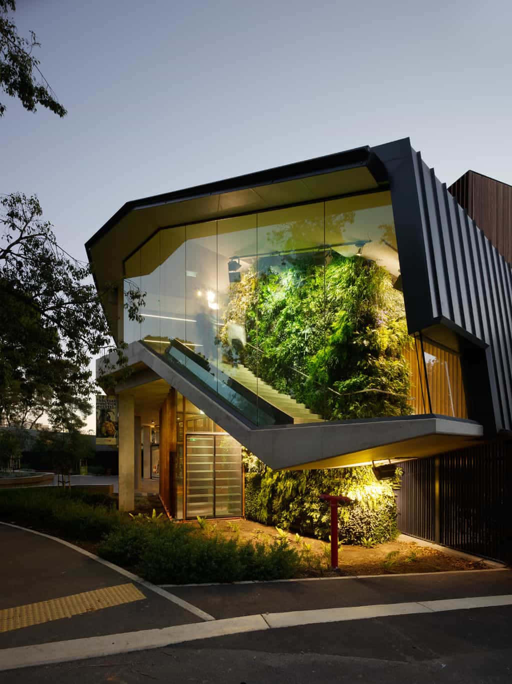 Green Buildings 桌布 壁紙 — 一座現代玻璃建築在黃昏時分設有發光的垂直花園和從內部照亮的浮動樓梯。