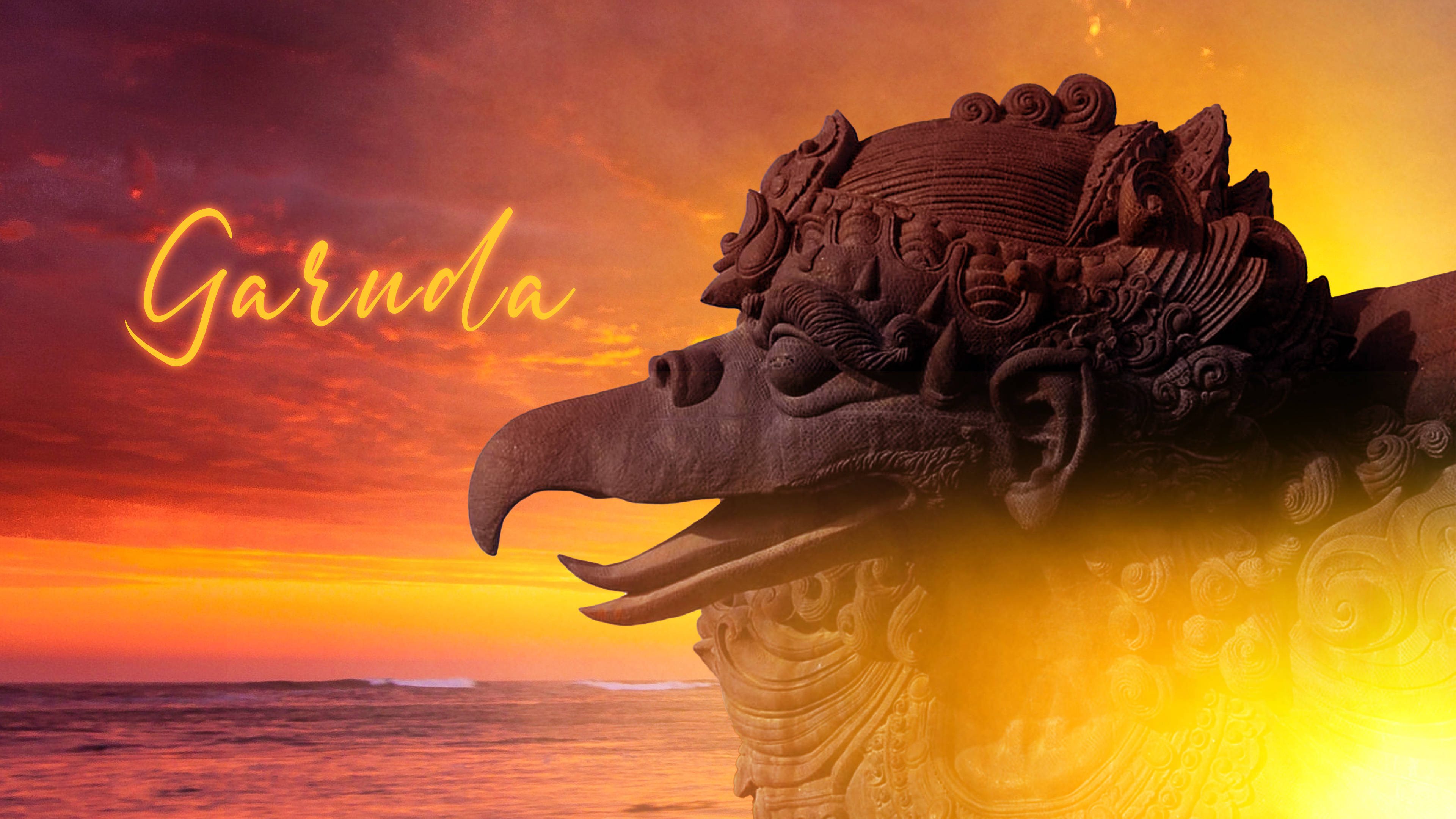 Garuda 桌布 壁紙 — 一座用深色石頭雕刻而成的雄偉迦樓羅雕像，矗立在海洋上熾熱的日落和發光的橙色和紅色雲彩前。