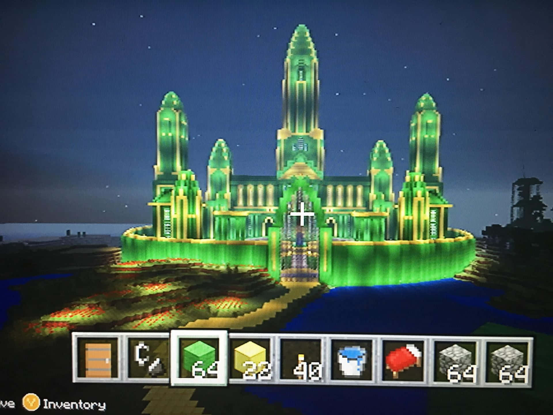 Minecraft Emeralds 桌布 壁紙 — 一座發光的綠色像素城堡在Minecraft遊戲世界中，在星空和庫存覆蓋層下，於夜晚雄偉地聳立。