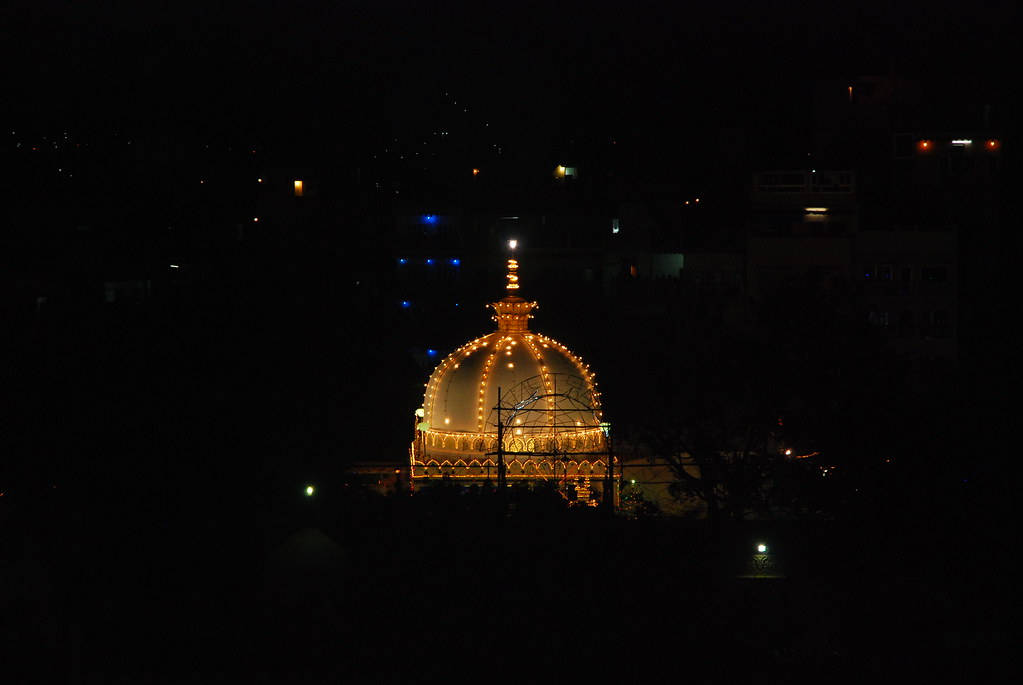Church 桌布 壁紙 — 一座發光的金色圓頂寺廟在黑暗的夜空下，在剪影般的城市天際線上方亮起。