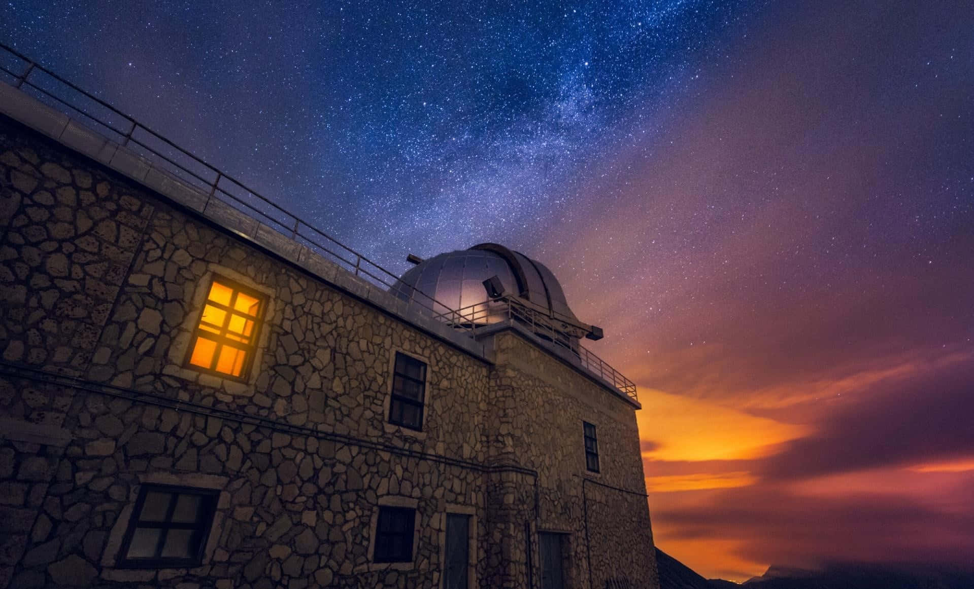 Space Observation 桌布 壁紙 — 一座石造天文台，帶有發光的窗戶和圓頂，矗立在佈滿夕陽色彩的星空下。