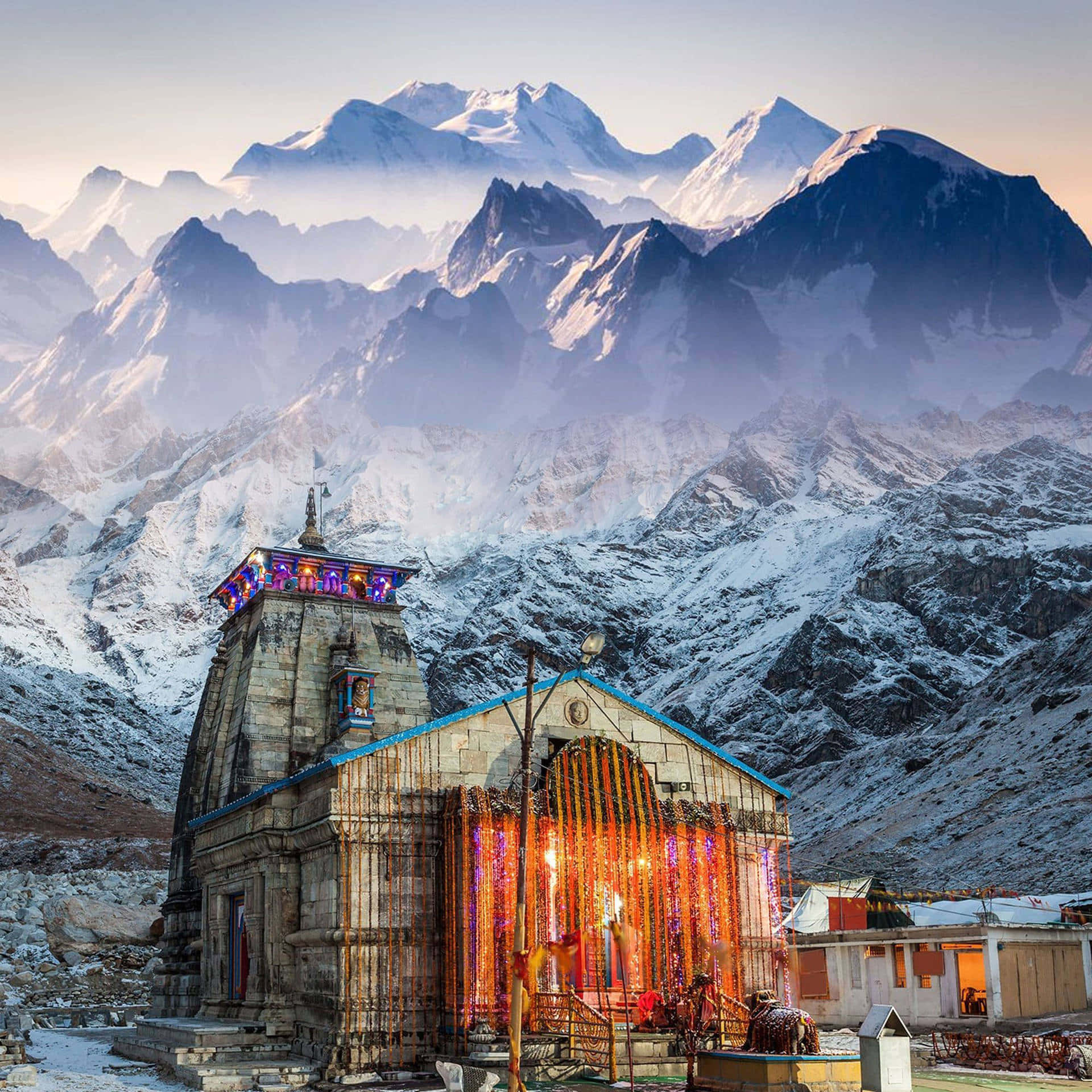 Kedarnath 桌布 壁紙 — 一座積雪的山中寺廟在霧濛濛的黎明天空中閃爍著五彩燈光。