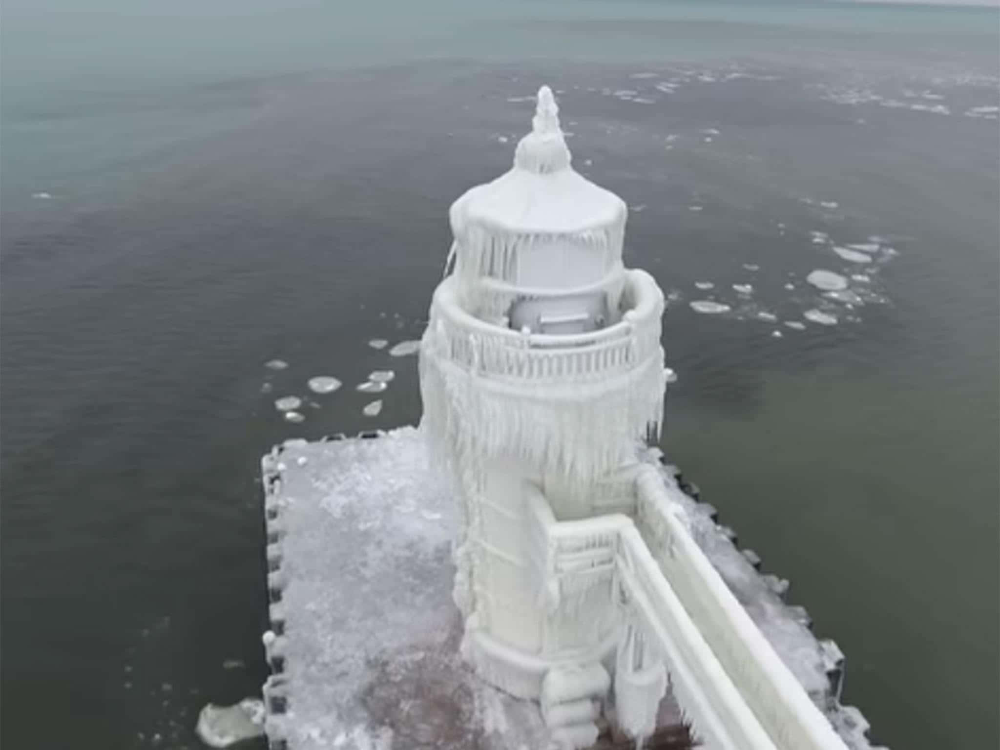 Polar Vortex 桌布 壁紙 — 一座被厚冰和冰柱覆蓋的冰凍燈塔孤獨地矗立在冰凍的碼頭上，四周是冰冷的海水。