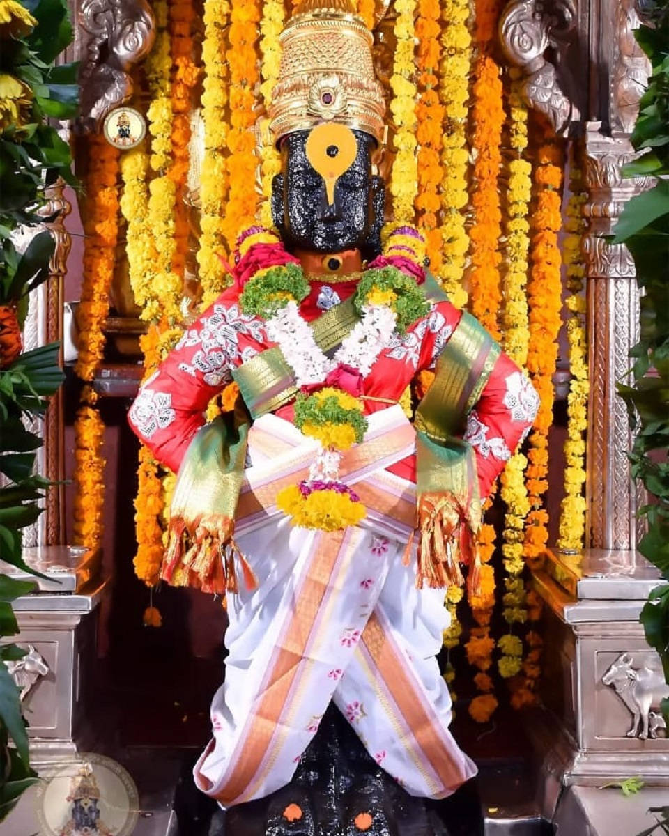 Hindu Temple 桌布 壁紙 — 一座裝飾華麗的黑色神像，披著紅、白、金色的布料，掛著萬壽菊花環，背景是華麗的寺廟。