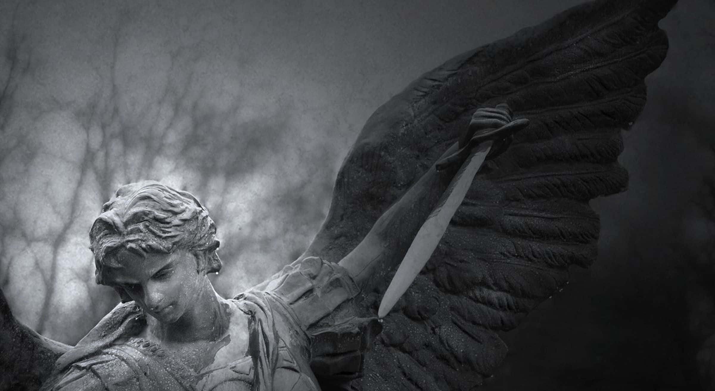 Saint Michael 桌布 壁紙 — 一座陰鬱的石天使雕像展開翅膀，手持劍，背景是霧氣瀰漫的荒蕪樹木。