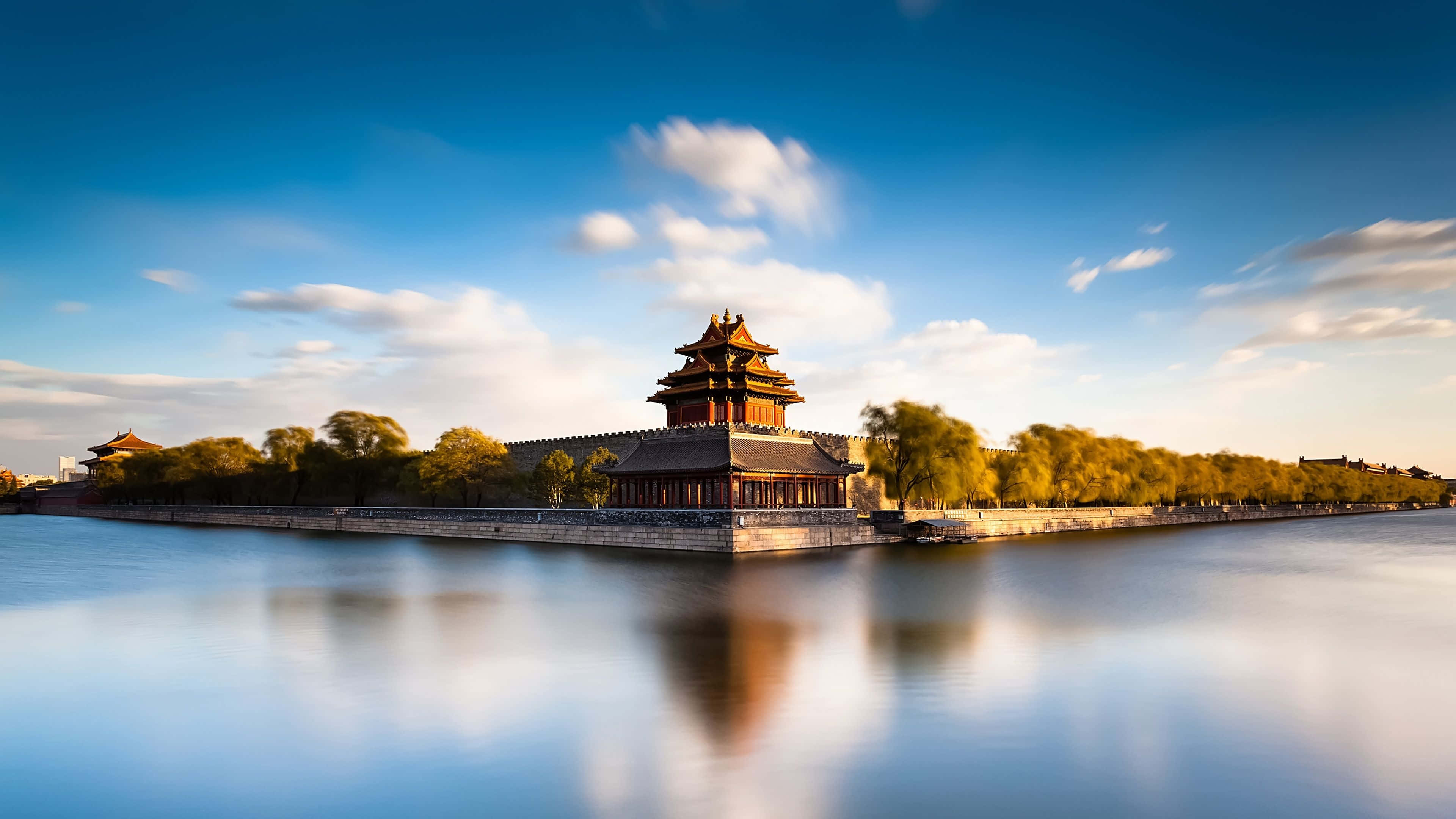 3d Travel 桌布 壁紙 — 一座雄偉的傳統中式宮殿塔樓矗立在平靜河流中的石島上，上方是帶有柔和雲朵的鮮豔藍天。