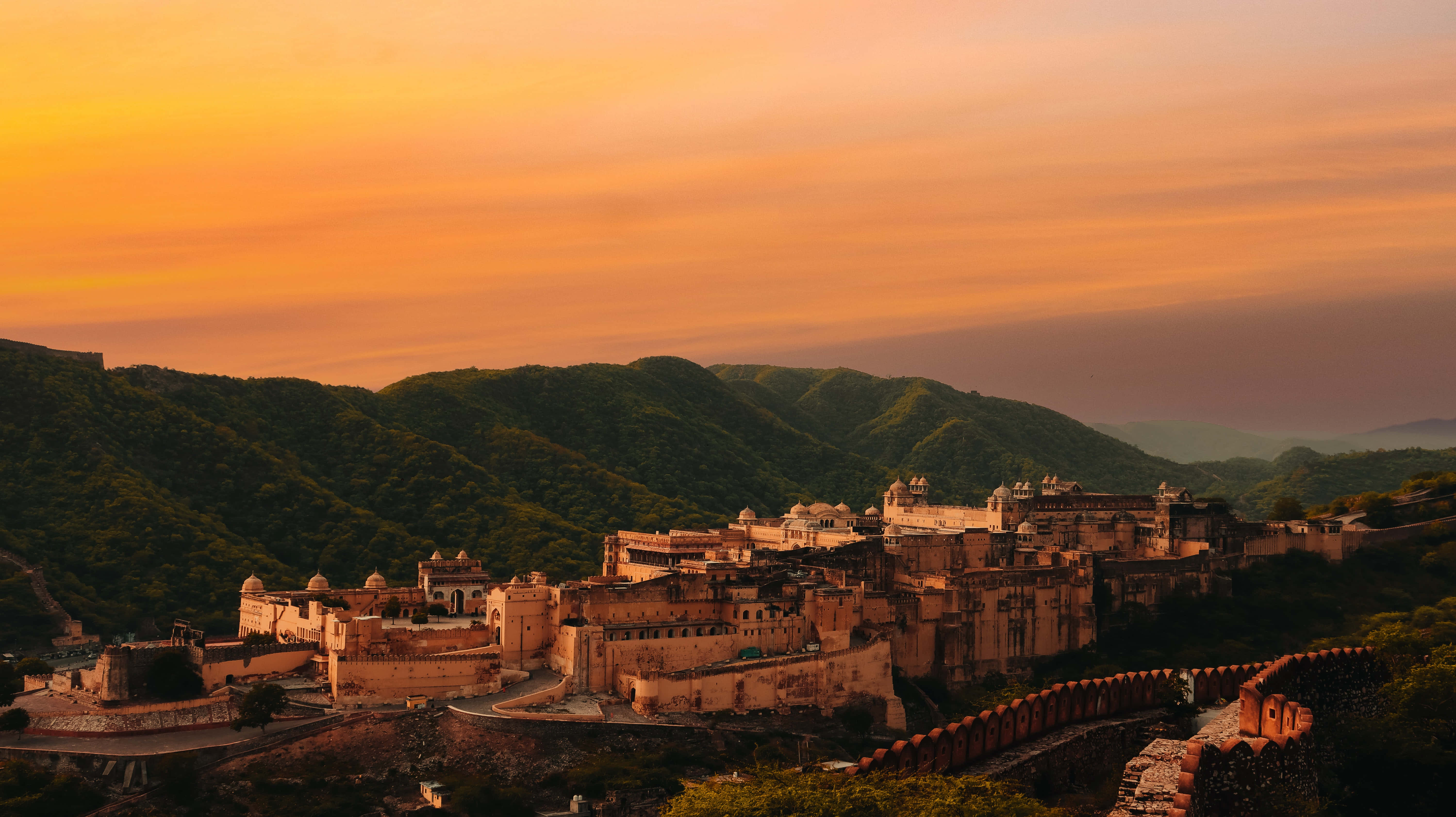 Rajasthan 桌布 壁紙 — 一座雄偉的古老堡壘坐落在翠綠的山丘上，沐浴在溫暖的金色日落光芒中。