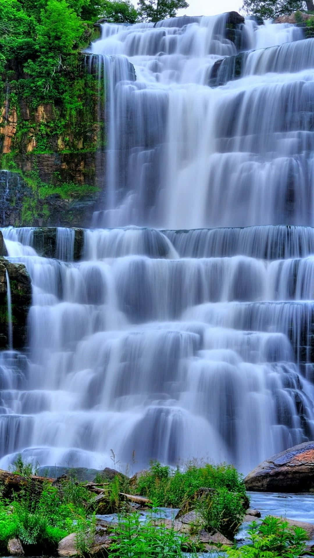 3d Waterfall 桌布 壁紙 — 一座雄偉的多層瀑布從長滿苔蘚的岩石上傾瀉而下，四周環繞著鬱鬱蔥蔥的綠色森林。