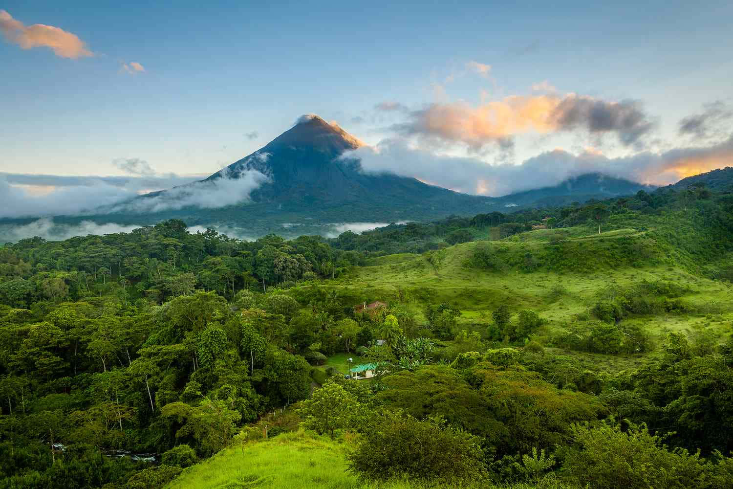 Costa Rica 桌布 壁紙 — 一座雄偉的火山在金色日出時升起於霧氣瀰漫的綠色山丘和茂密叢林之上。