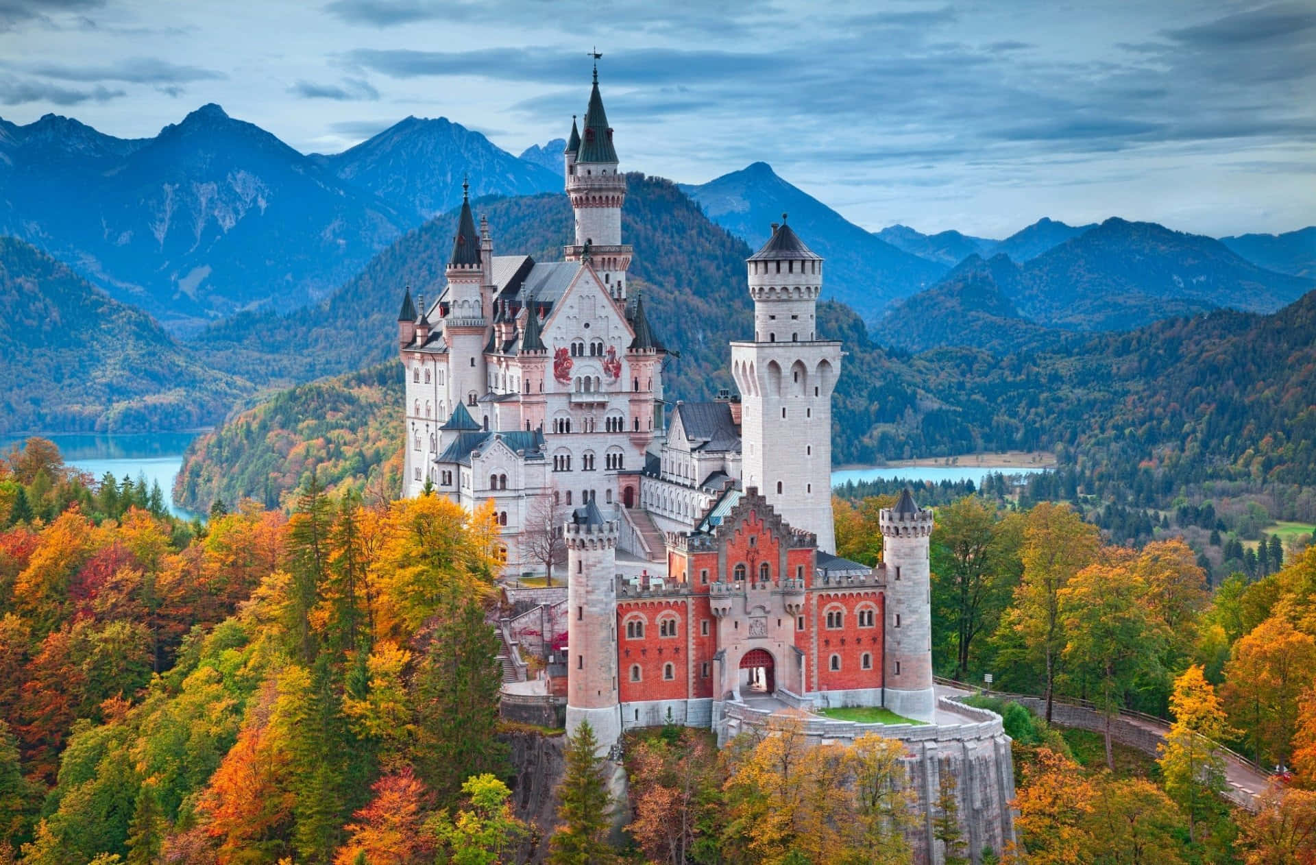 Germany 桌布 壁紙 — 一座雄偉的童話城堡坐落在懸崖上，周圍是生機勃勃的秋日森林和遠山，天空多雲。