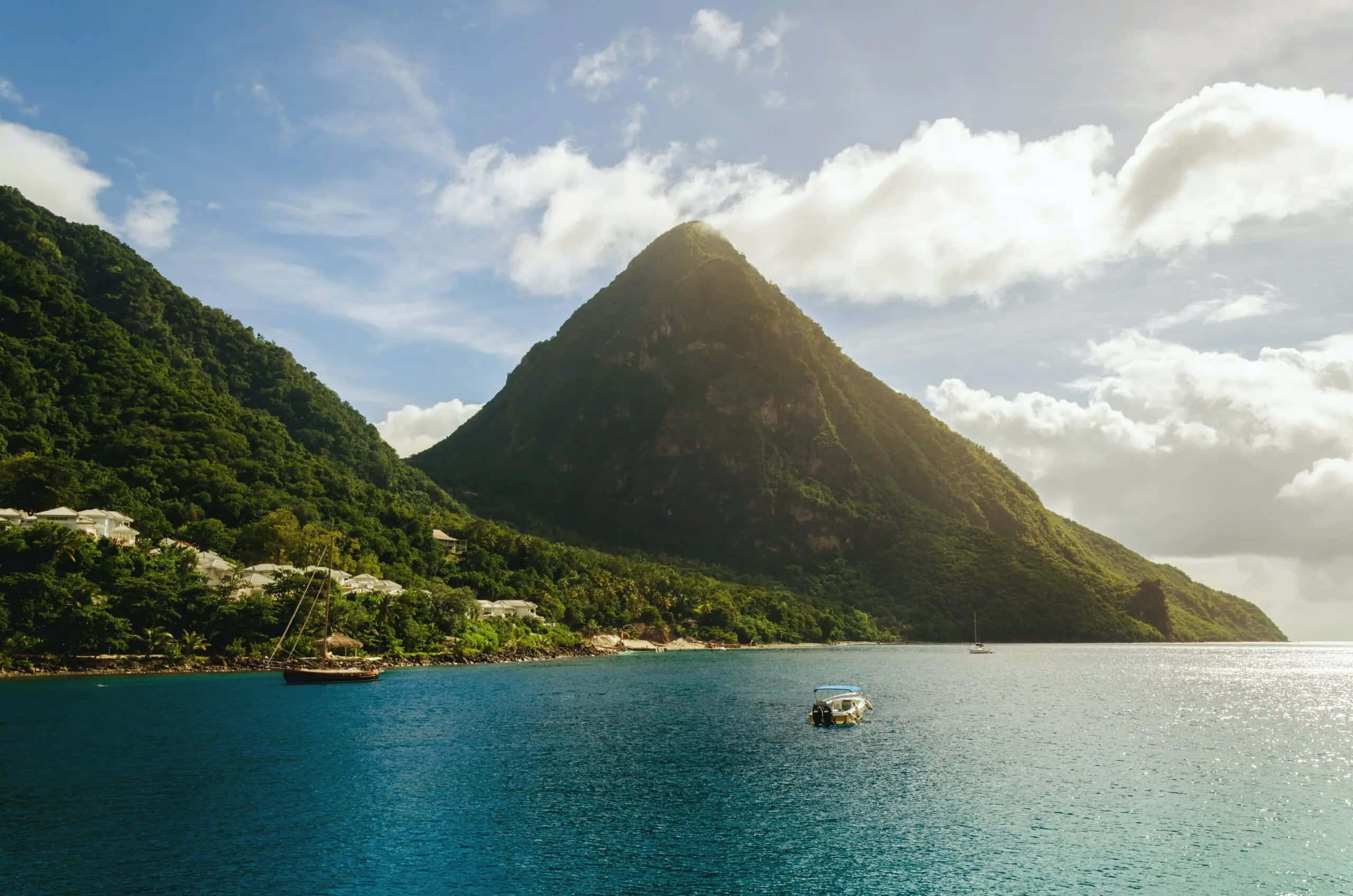 Caribbean 桌布 壁紙 — 一座雄偉的綠色山峰從碧綠的海水中升起，上方是明亮的藍天和蓬鬆的白雲。