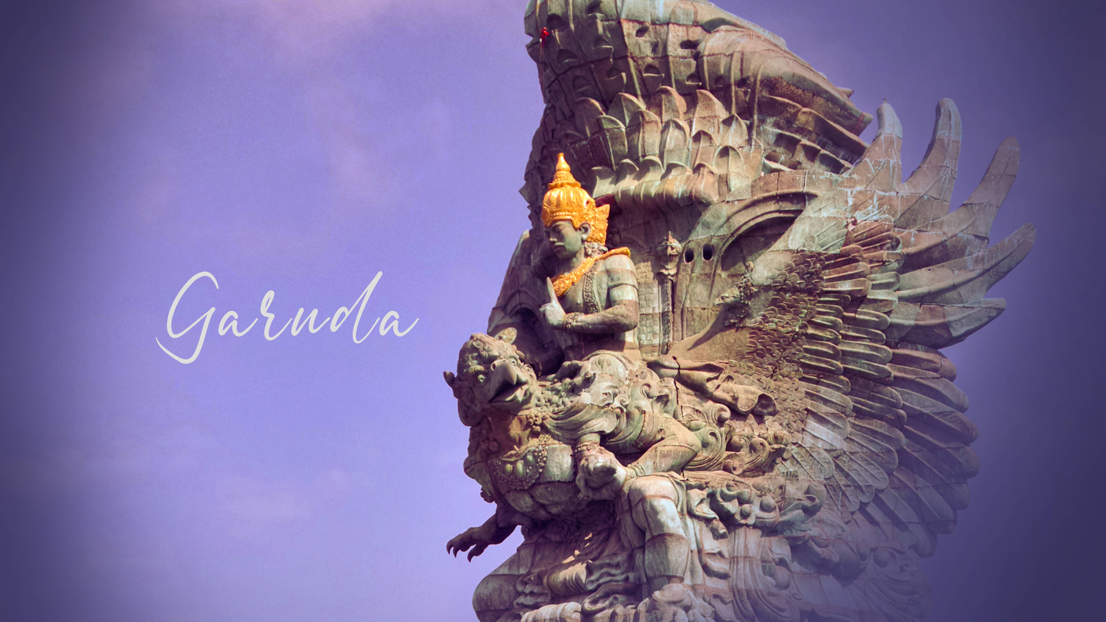 Vishnu 桌布 壁紙 — 一座雄偉的迦樓羅雕像，頭戴金色皇冠，翅膀細節精緻，矗立在柔和的紫色天空背景下。