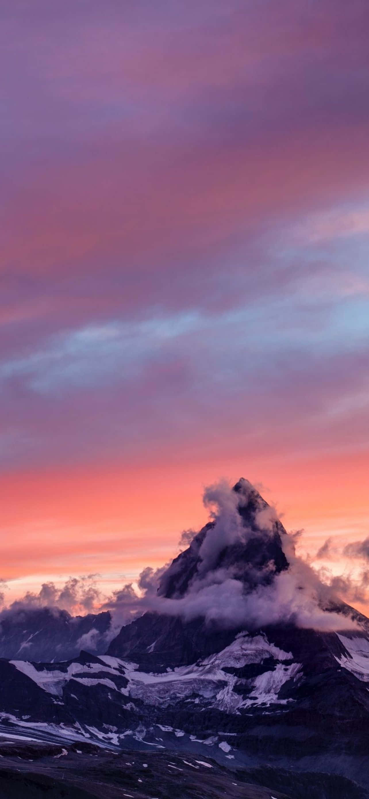Mountain iPhone 桌布 壁紙 — 一座雄偉的雪山峰頂刺穿充滿活力的粉紅色和紫色日落天空，縷縷雲彩在其頂峰周圍盤旋。