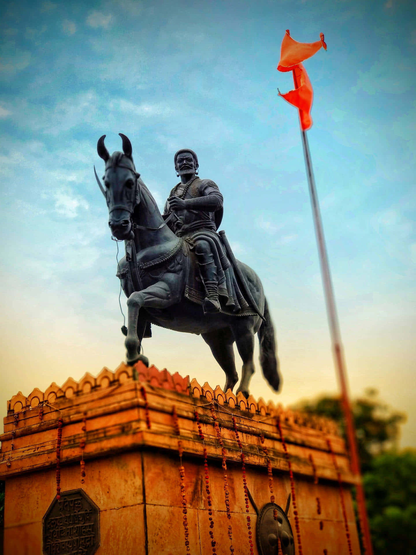 Shivaji Maharaj 桌布 壁紙 — 一座雄偉的青銅騎馬戰士雕像，立於石基座上，一面橙色旗幟在暮色天空中飄揚。