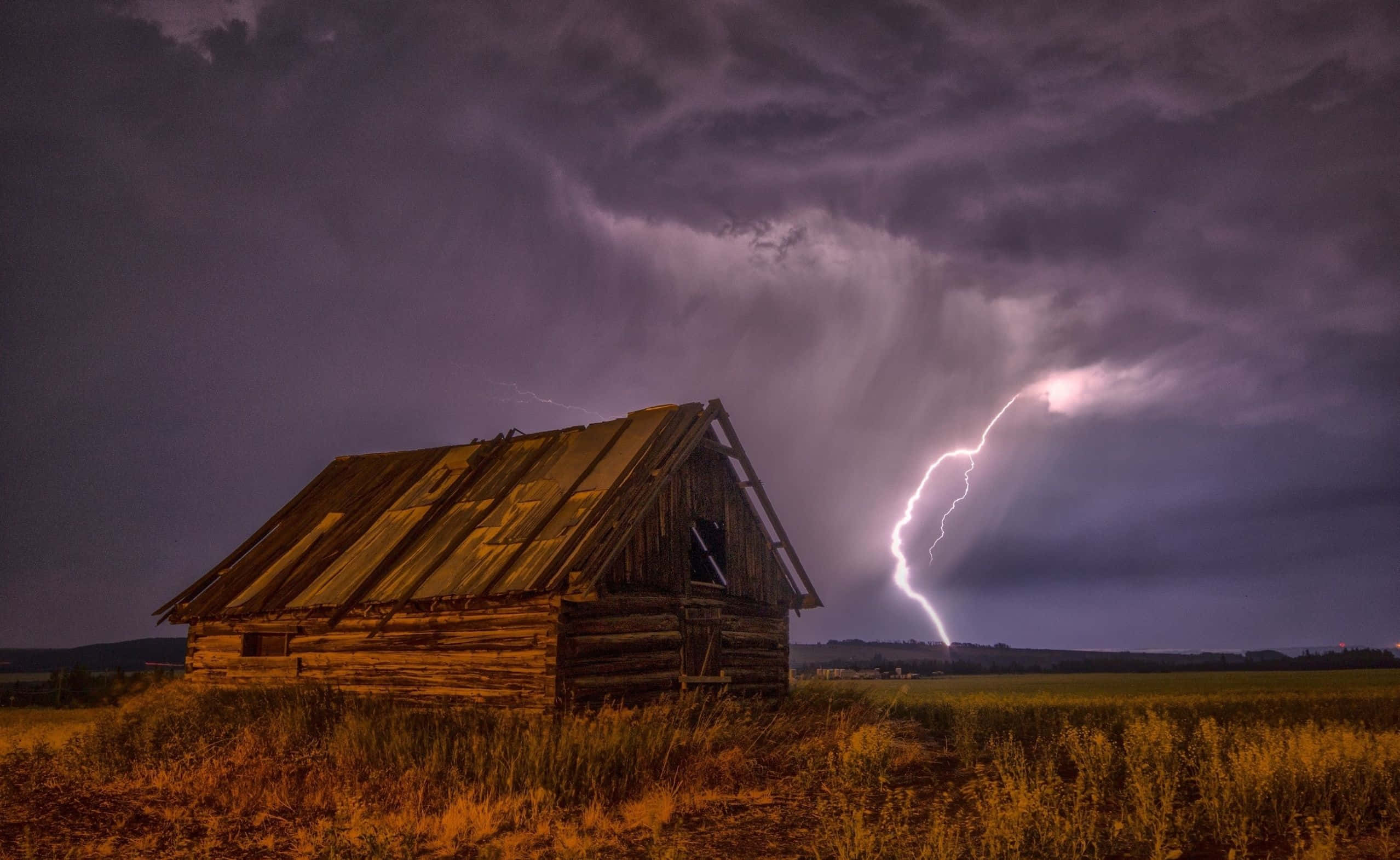 Thunderstorm 桌布 壁紙 — 一座風化的木屋孤零零地矗立在田野中，一道明亮的閃電在暴風雨紫色天空下劃過地平線。