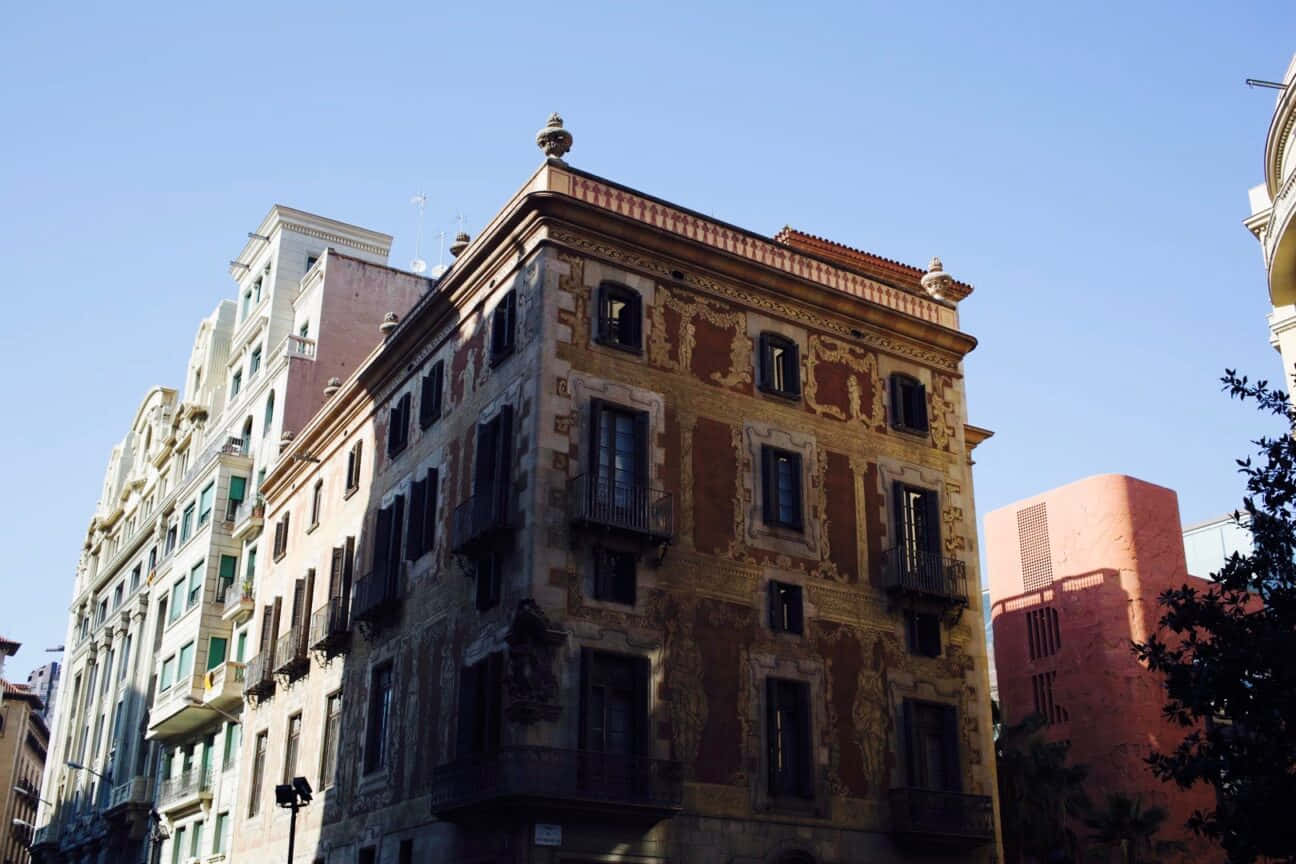巴塞隆拿 桌布 壁紙 — 一座風化的歷史建築，帶有華麗的陽台和褪色的壁畫，在晴朗的藍天下，矗立在陽光普照的城市環境中。