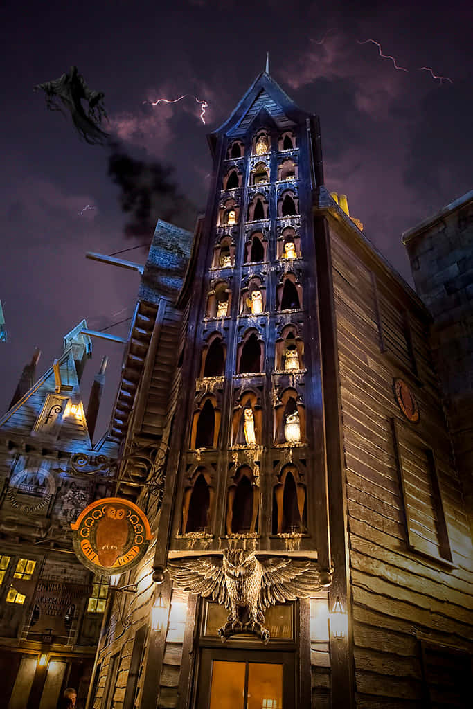 The Hogwarts Owlery 桌布 壁紙 — 一座高聳的哥德式建築，帶有發光的窗戶和一個大型貓頭鷹雕像，背景是雷電交加的暴風雨夜空。
