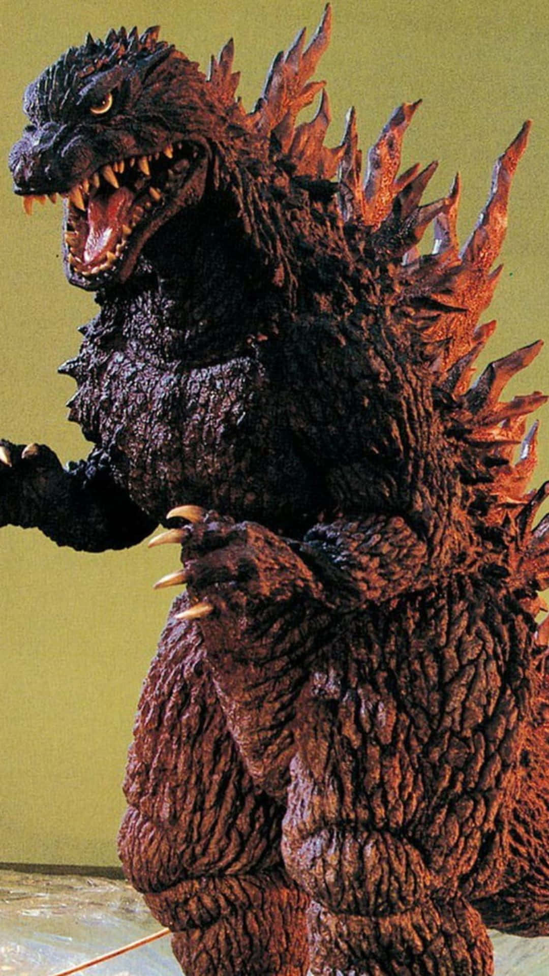 Godzilla 2000 桌布 壁紙 — 一座高聳的哥斯拉雕像，帶有紋理的深色鱗片和發光的眼睛，在純黃色牆壁前威嚴地站立。