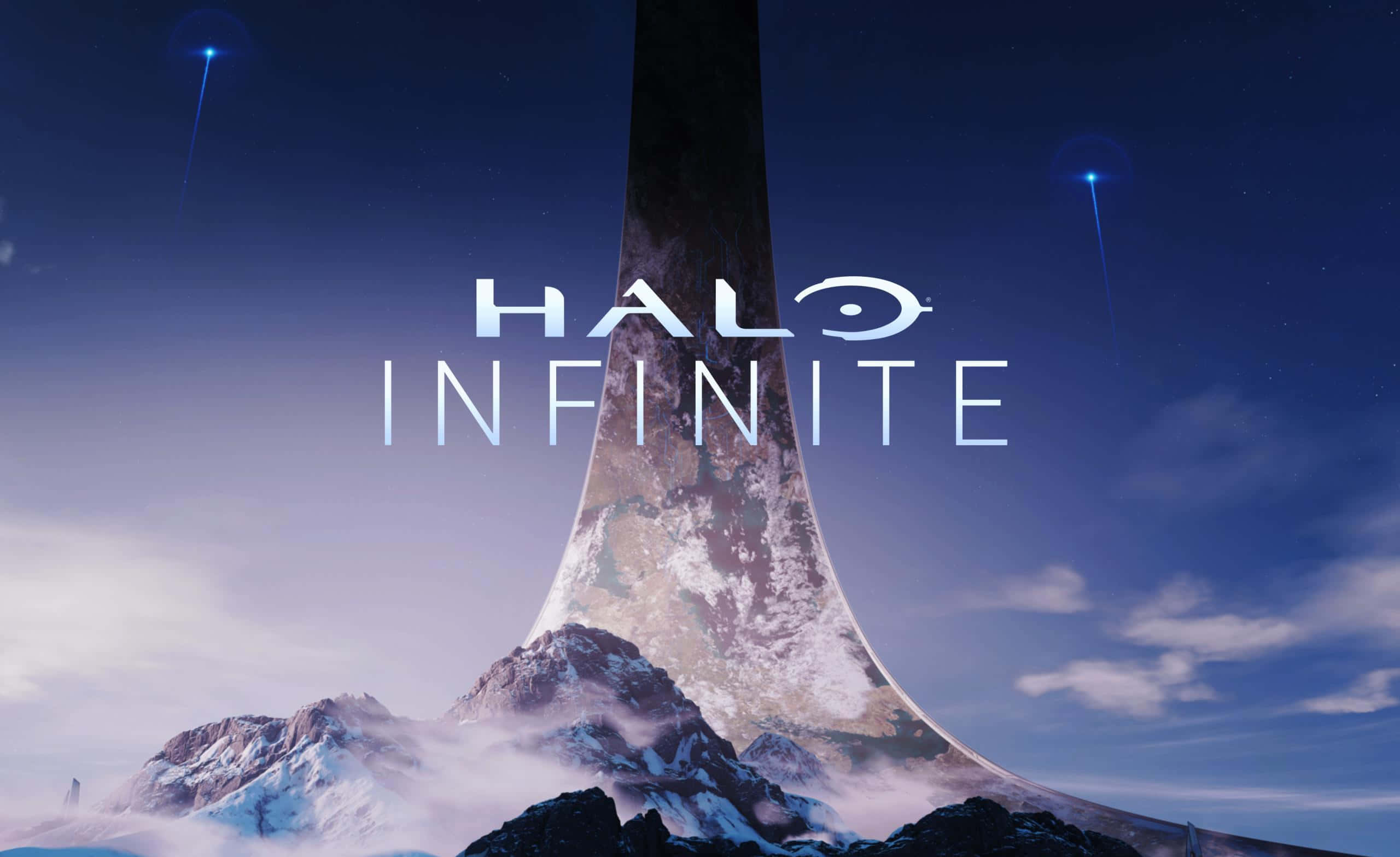Halo Ark 桌布 壁紙 — 一座高聳的巨石結構從白雪覆蓋的山脈中升起，在暮色天空下散發出藍色光芒。