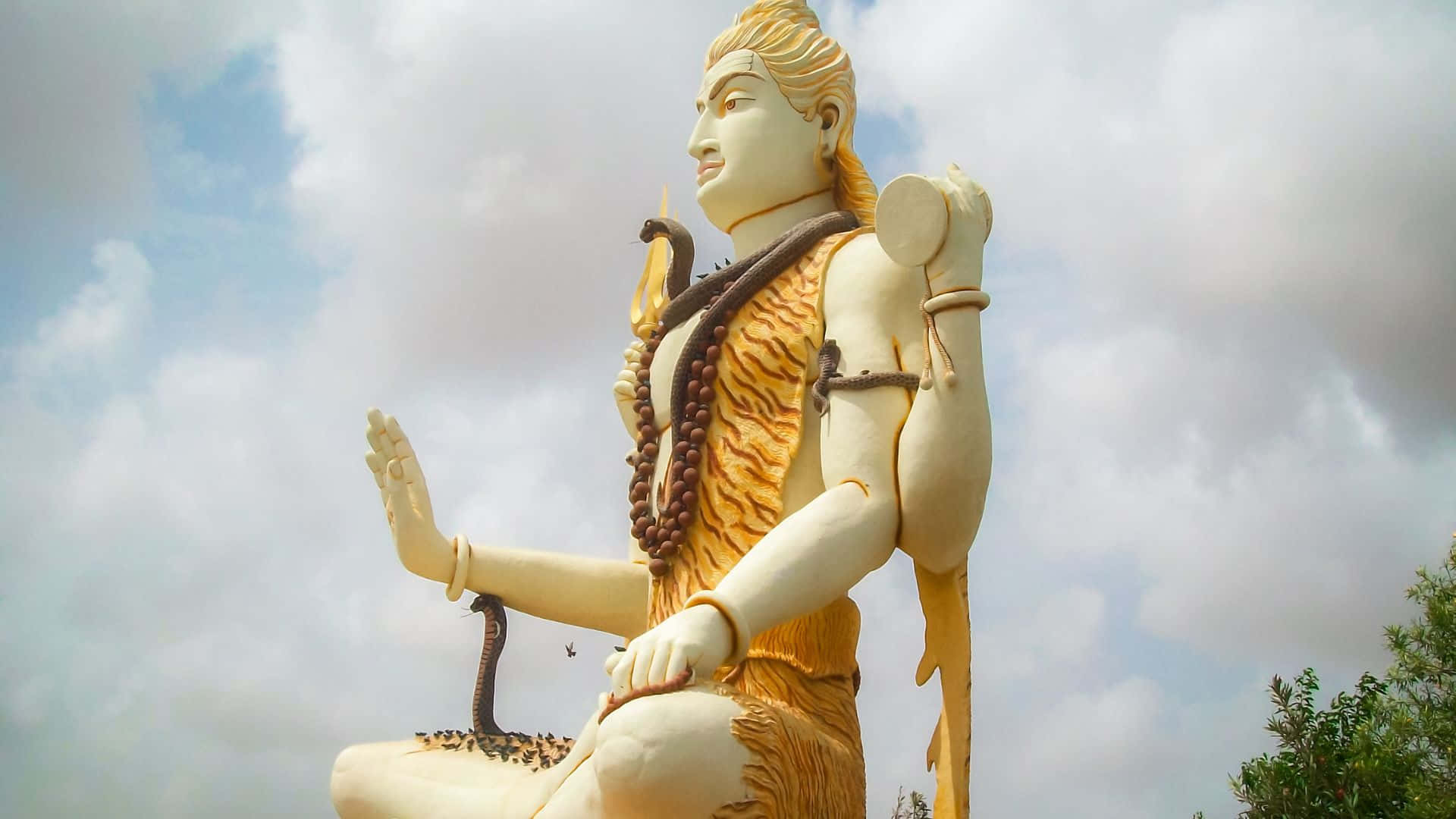 Shiva 桌布 壁紙 — 一座高聳的白色濕婆神像，腰間圍著虎皮，頸上纏著蛇，矗立在多雲的天空下。