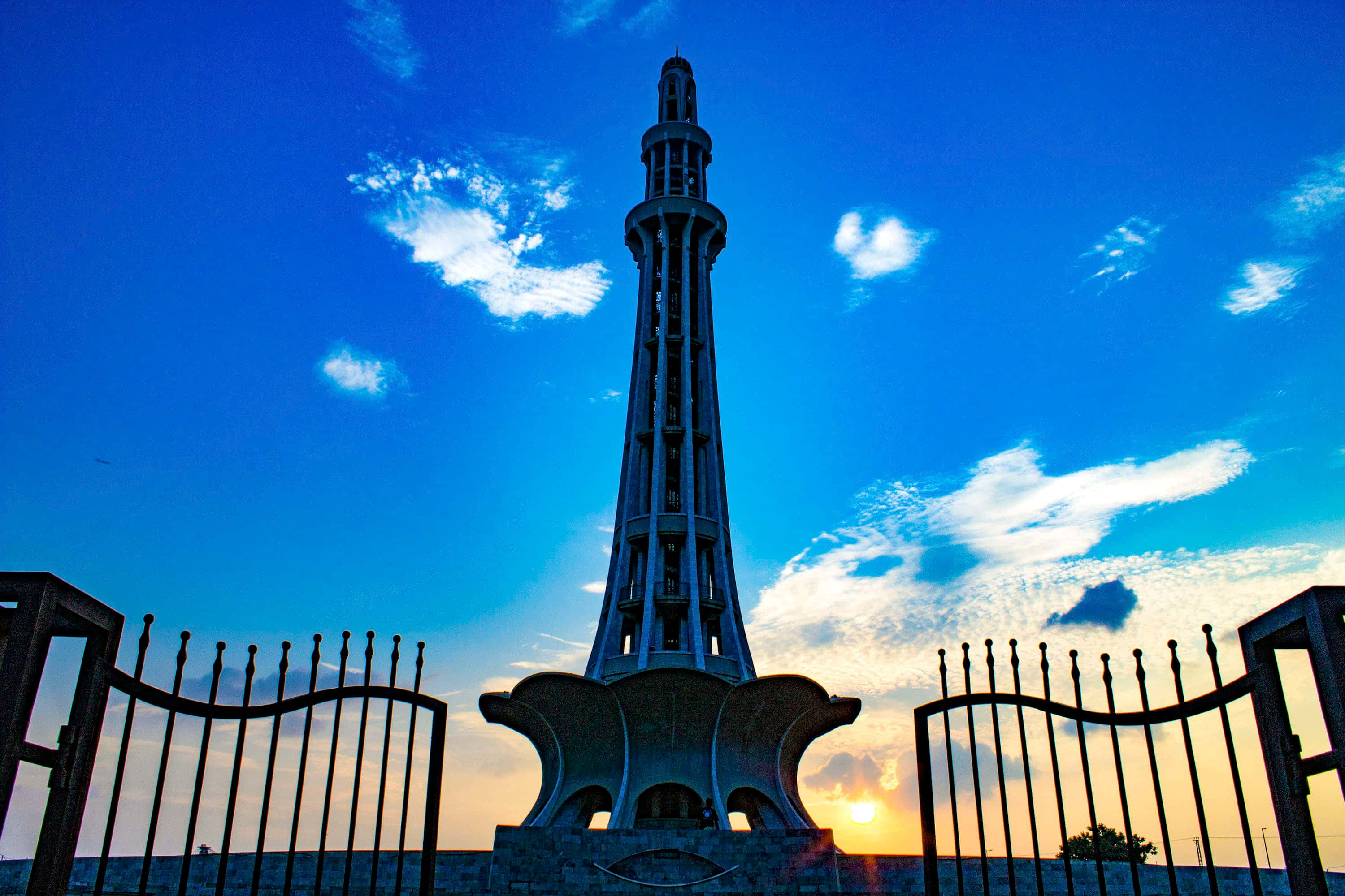 Pakistan 桌布 壁紙 — 一座高聳的紀念碑在夕陽西下時，以藍天白雲為背景形成剪影。