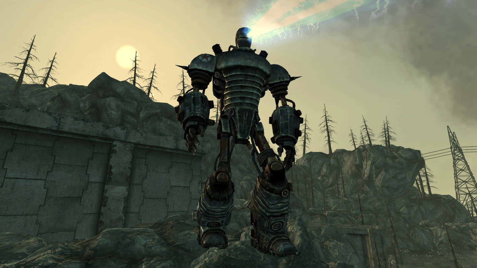 Liberty Prime 桌布 壁紙 — 一座高聳的裝甲動力裝甲服站在岩石地形上，天空朦朧，有發光的太陽和光禿禿的樹木。