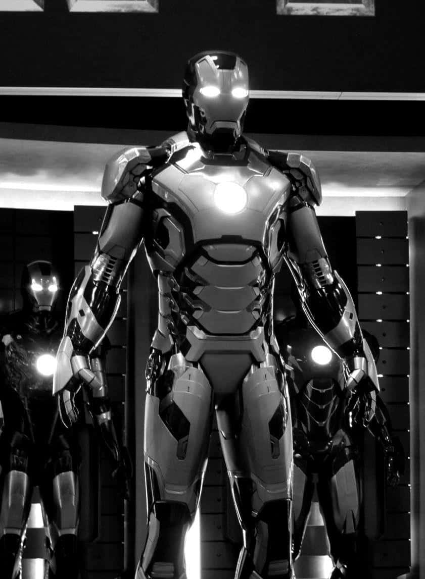 Iron Man Suit 桌布 壁紙 — 一座高聳的鐵甲奇俠裝甲在單色燈光下矗立，兩側還有另外兩套裝甲，位於高科技艙室中。