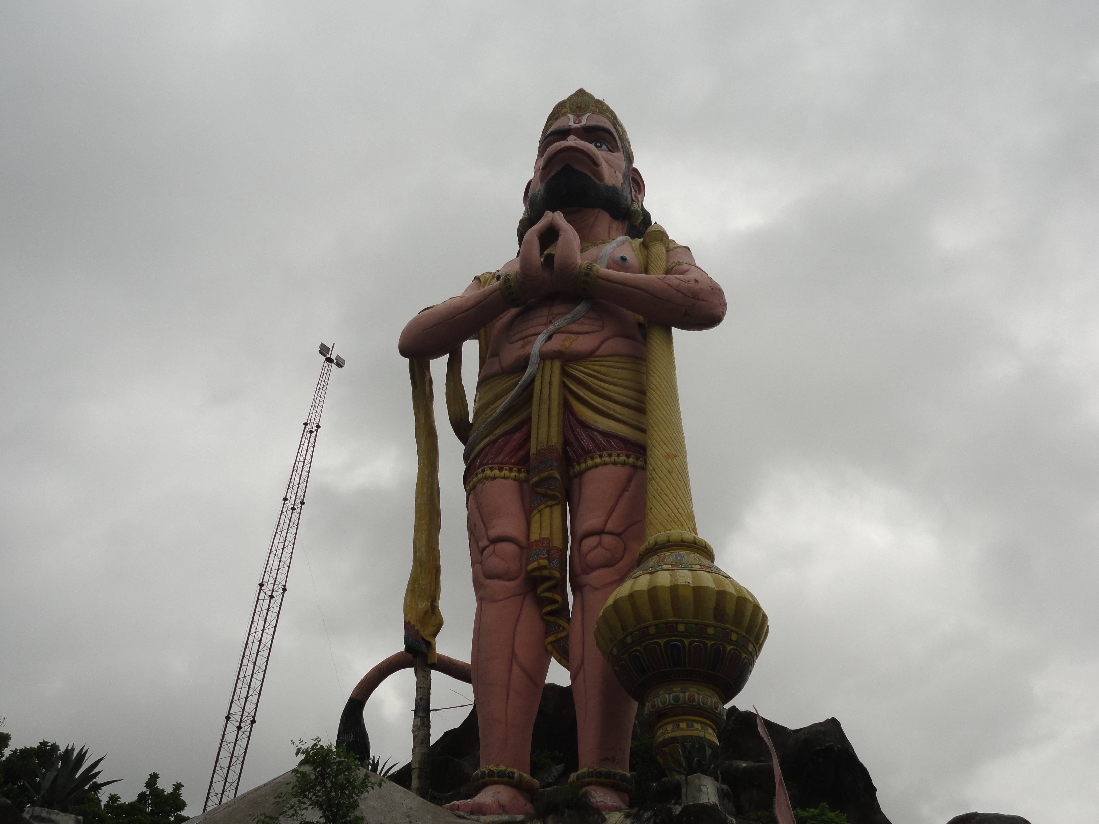 statue 桌布 壁紙 — 一座高聳的雕像，描繪一位留鬍鬚、戴皇冠的肌肉神祇，在陰雲密佈的天空下手持金色權杖。