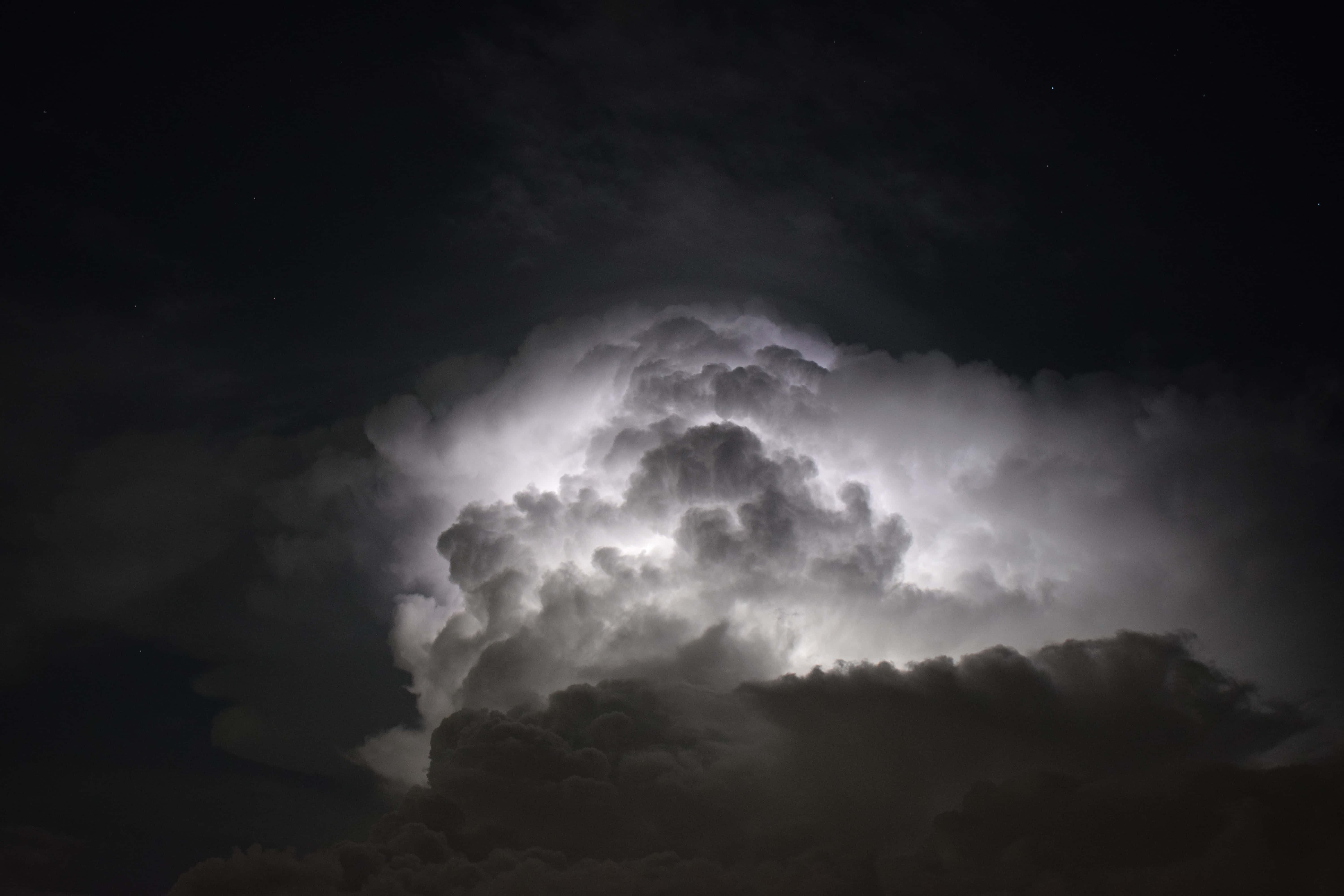 唯美雲朵 桌布 壁紙 — 一座高聳的風暴雲，內部被閃電照亮，背景是繁星點點的夜空。