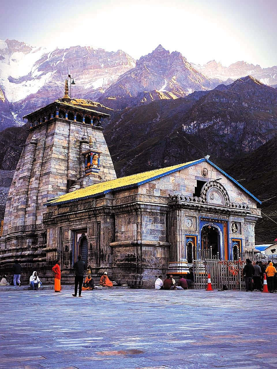 Kedarnath 桌布 壁紙 — 一座黃色屋頂的石廟矗立在雪山前，人們聚集在它的庭院中。