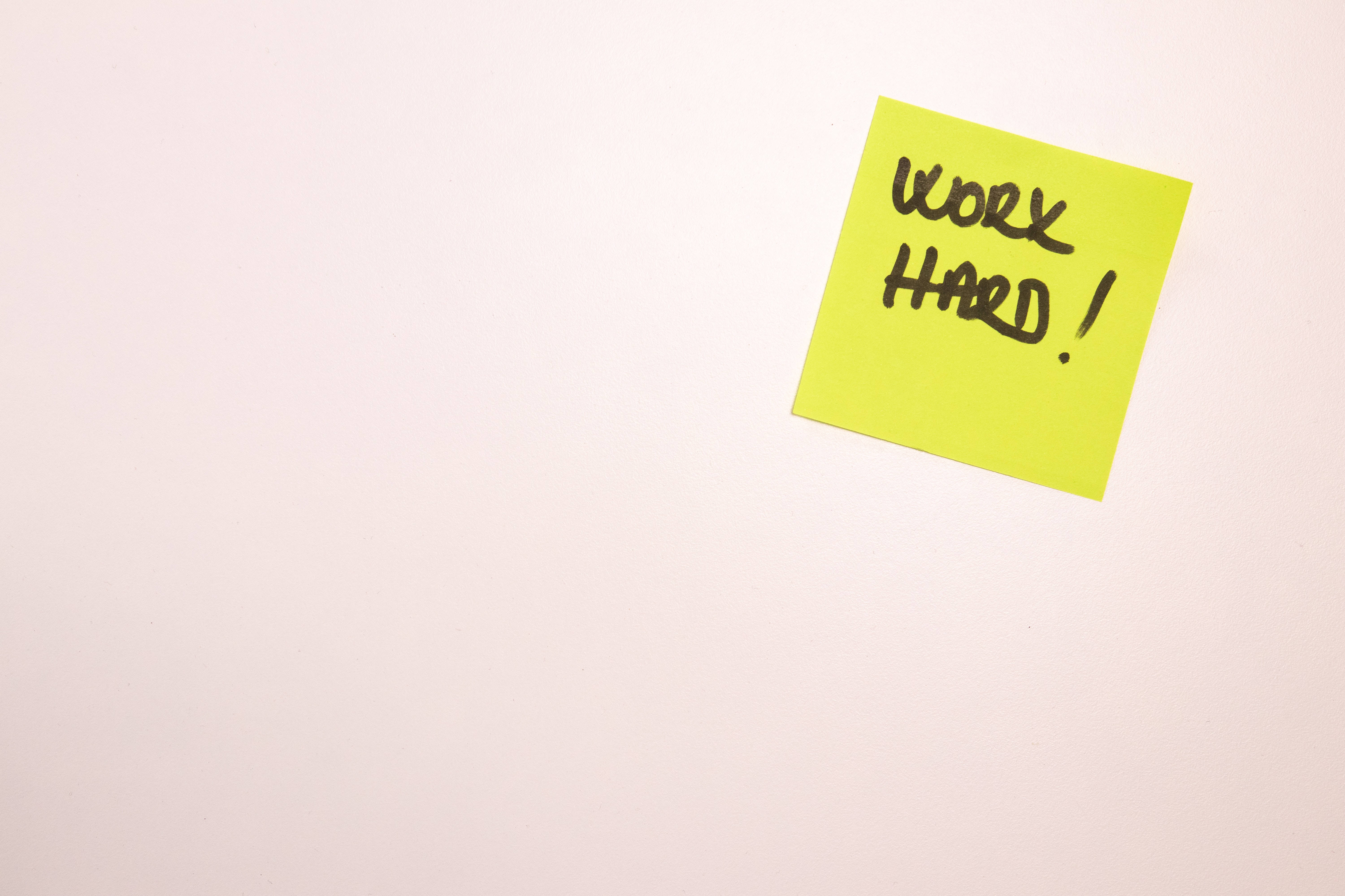 簡約 桌布 壁紙 — 一張亮黃色便利貼，上面有粗體手寫文字work hard，在純米白色背景上表達動力。