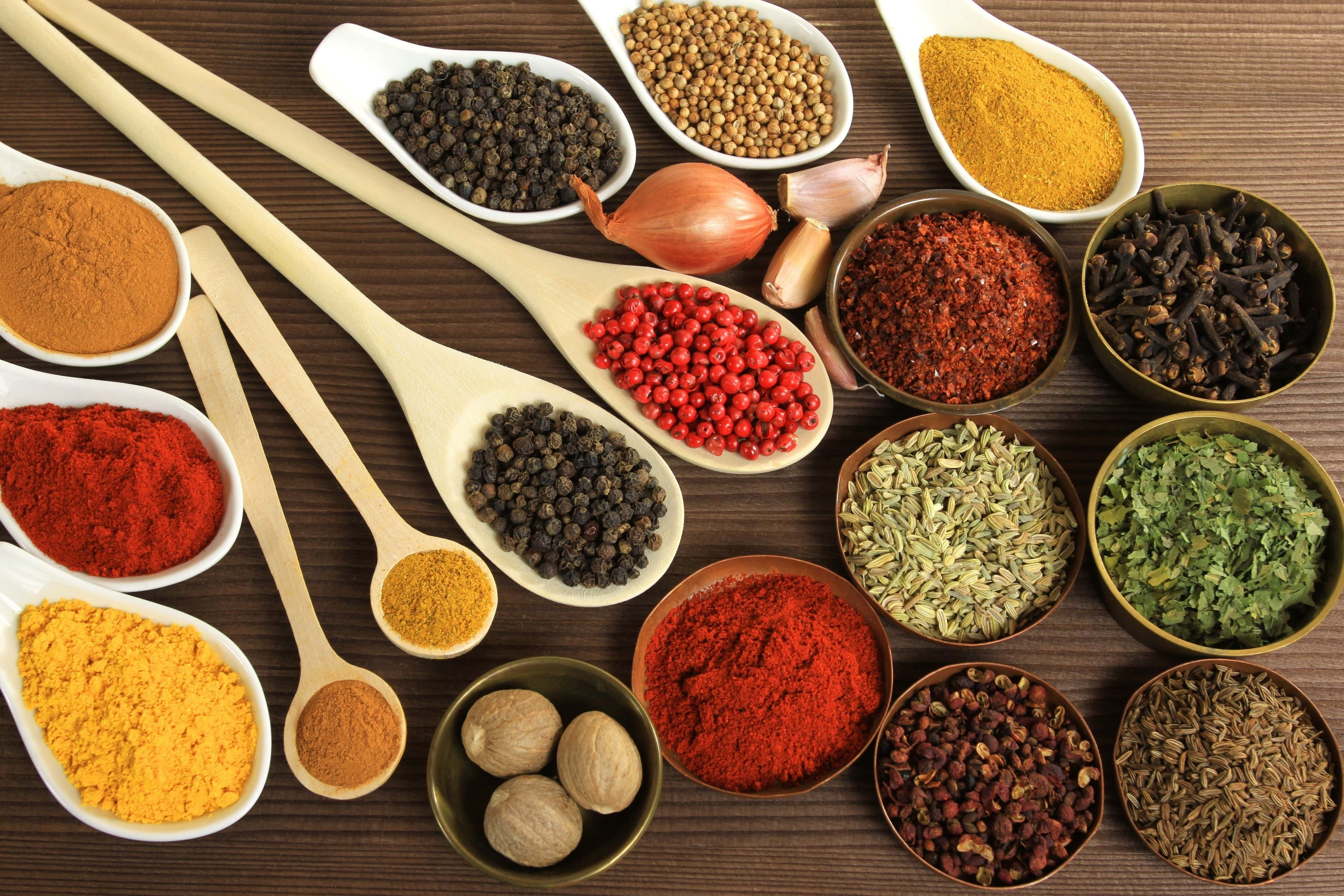 Indian Food 桌布 壁紙 — 一張充滿活力的俯拍照片，展示各種香料和調味料放在木勺和碗中，排列在深色木質表面上。