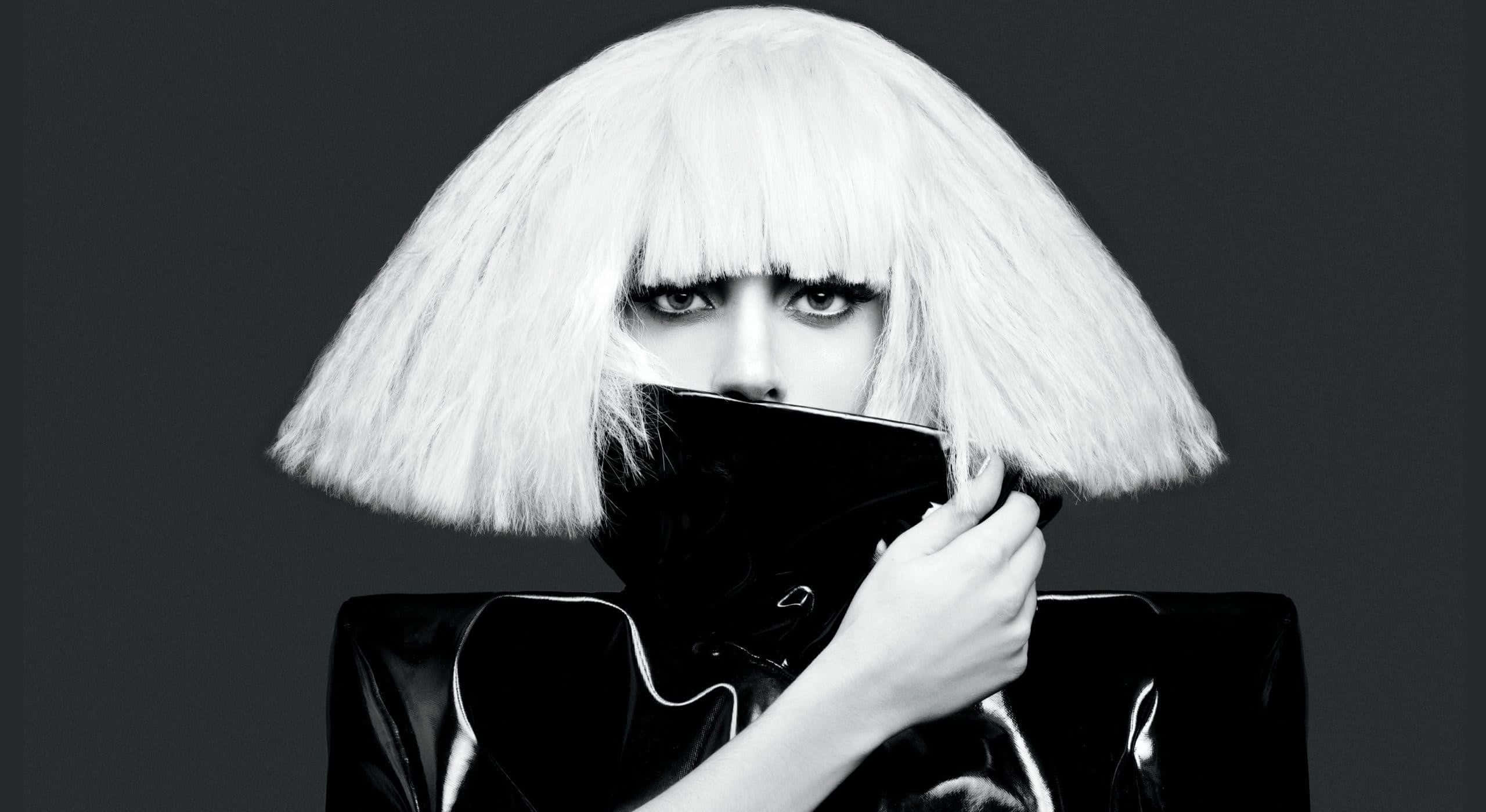 Lady Gaga 桌布 壁紙 — 一張引人注目的黑白肖像，人物戴著豐盈的白色鮑伯假髮，在深灰色背景前將黑色面具遮住嘴巴。