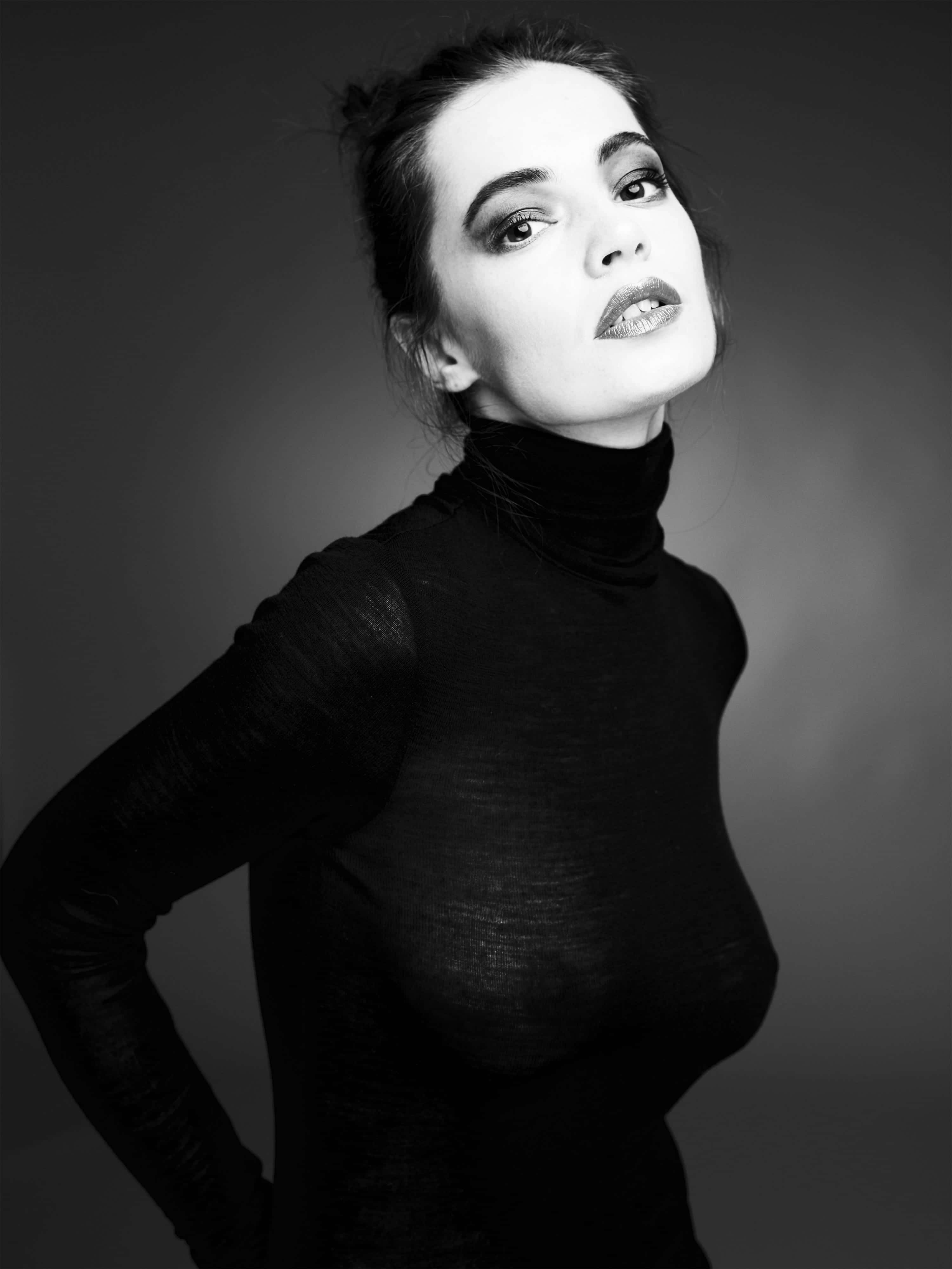 Black And White Fashion 桌布 壁紙 — 一張引人注目的黑白肖像照，一名身穿高領上衣的女性在灰色漸變背景前自信地擺姿勢。