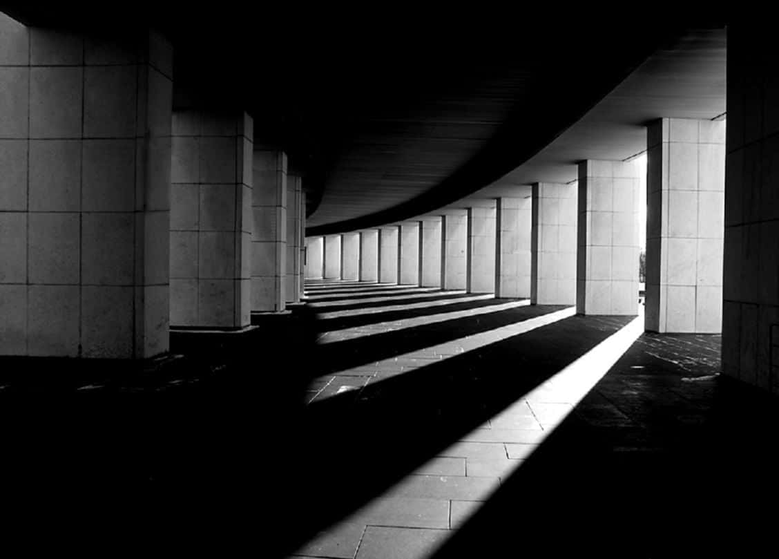 Black And White Architecture 桌布 壁紙 — 一張強烈黑白對比的照片，展示了一條彎曲的建築走廊，帶有強烈的幾何陰影和戲劇性的燈光。