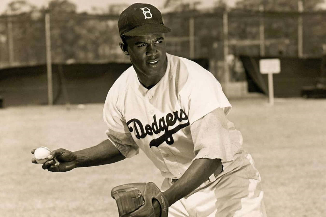 Jackie Robinson 桌布 壁紙 — 一張復古棕褐色調的照片，一名身穿道奇隊球衣的棒球選手在球場上拿著球和手套。