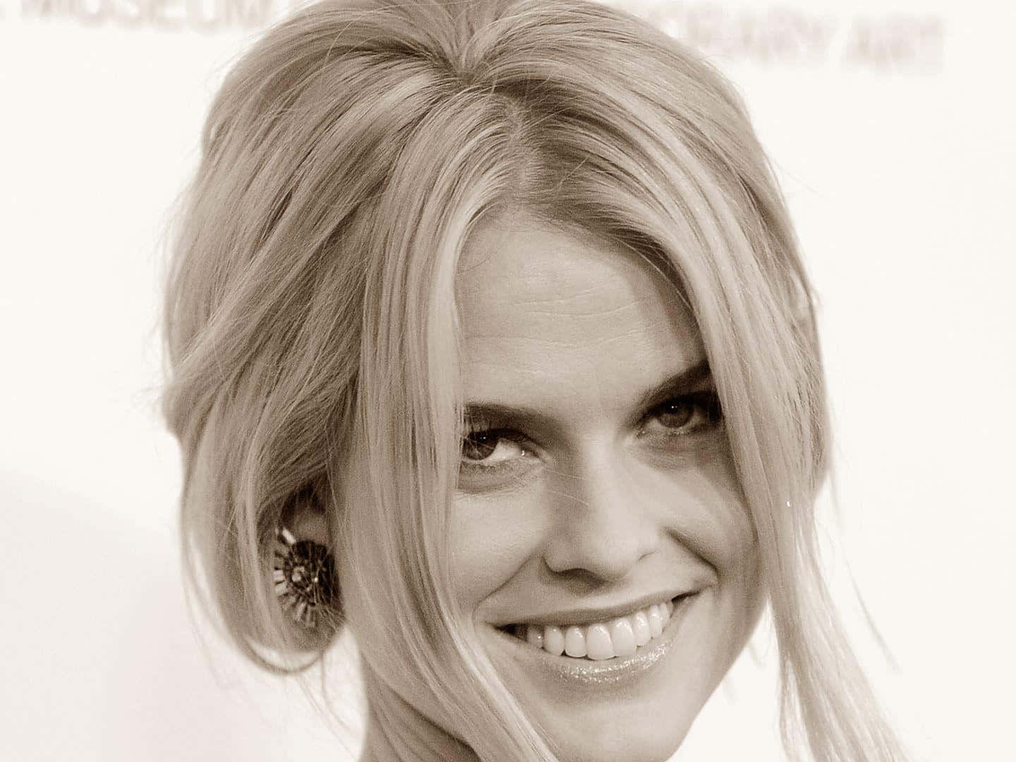 alice eve 桌布 壁紙 — 一張復古棕褐色調的特寫肖像，一位微笑的女性，擁有造型金髮和華麗耳環。