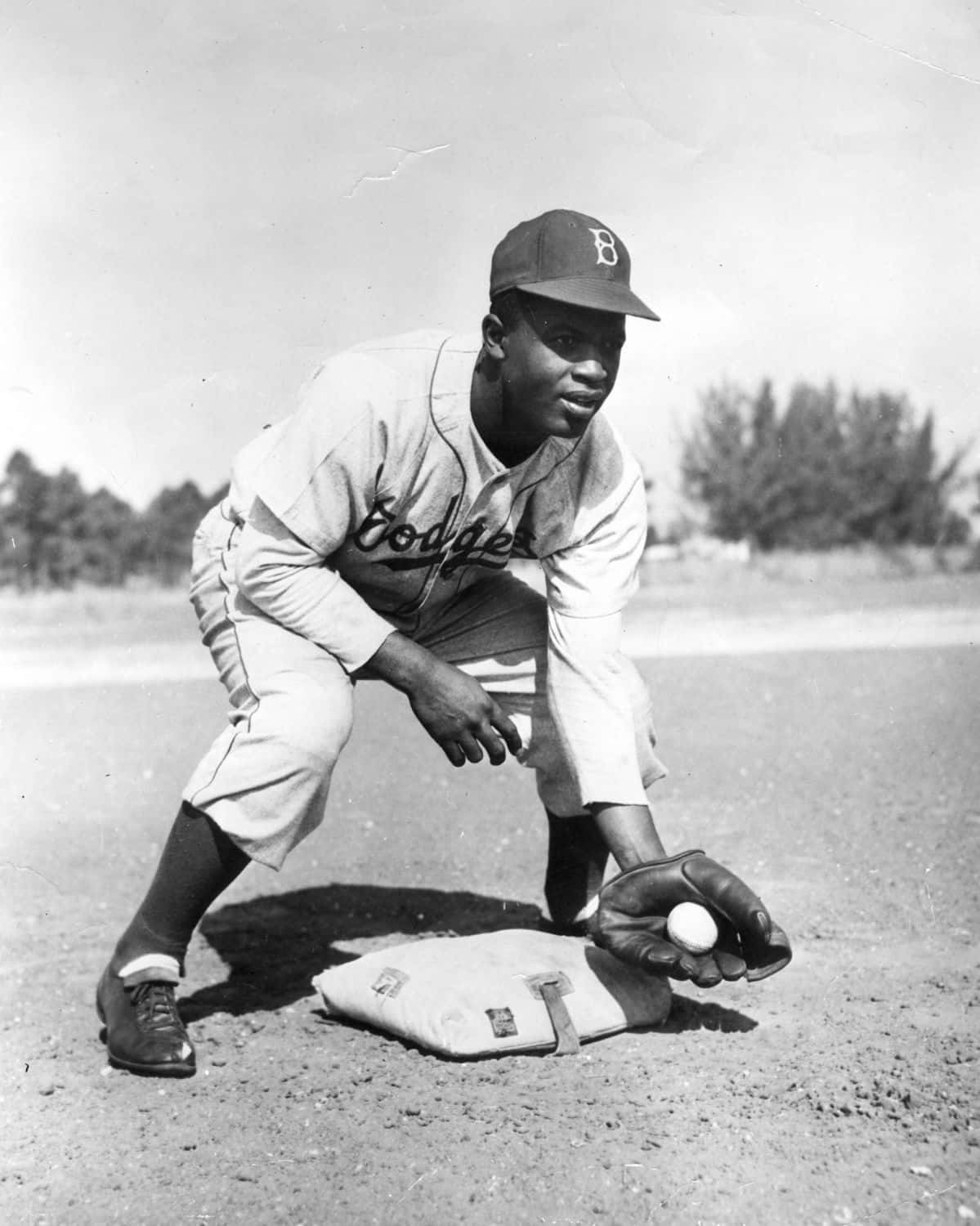 Jackie Robinson 桌布 壁紙 — 一張復古黑白照片，一名身穿道奇隊球衣的棒球選手蹲在本壘附近，戴著手套握著球。