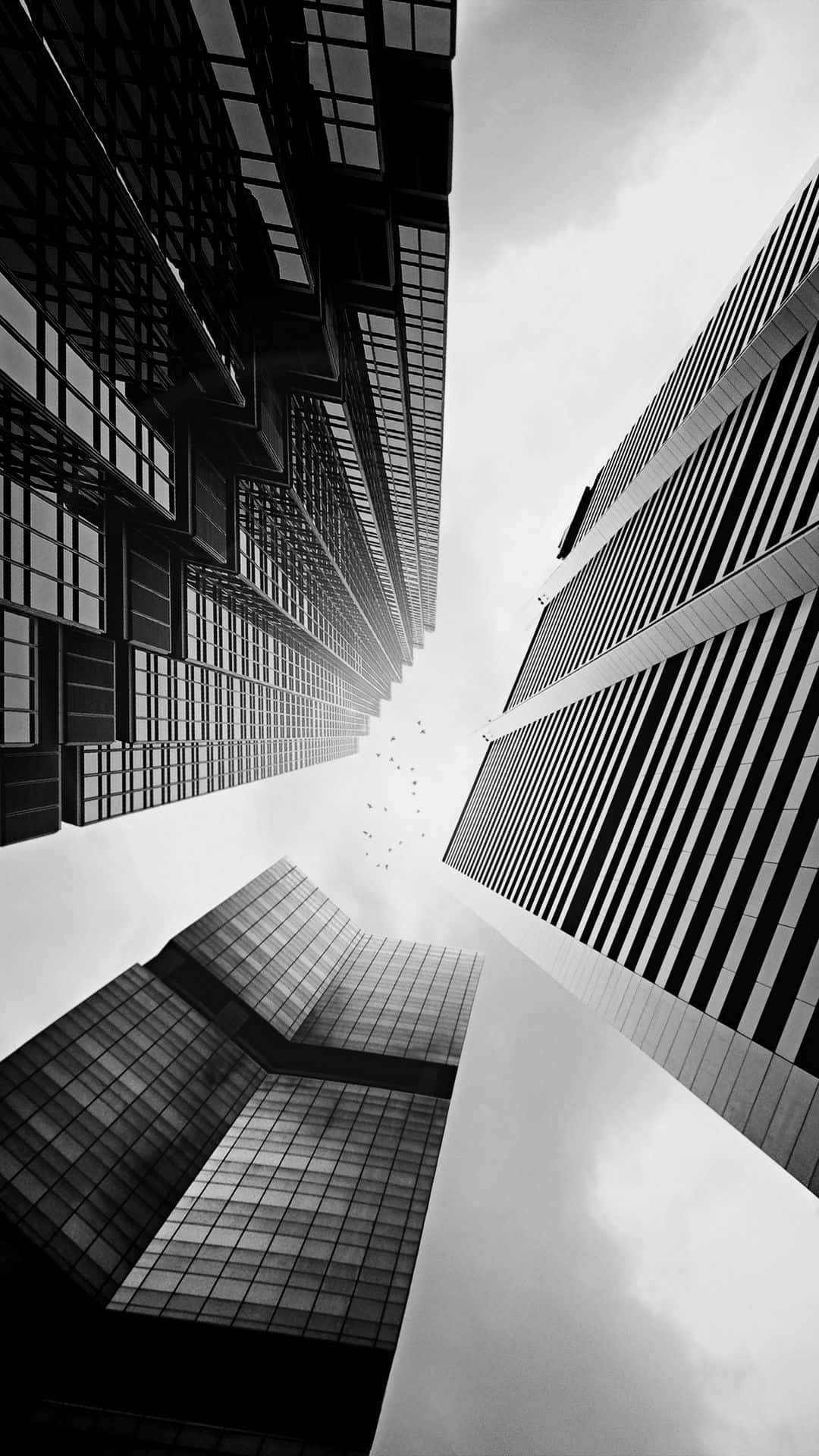 Black And White Architecture 桌布 壁紙 — 一張戲劇性的黑白低角度照片，拍攝高聳的摩天大樓向多雲的天空匯聚。