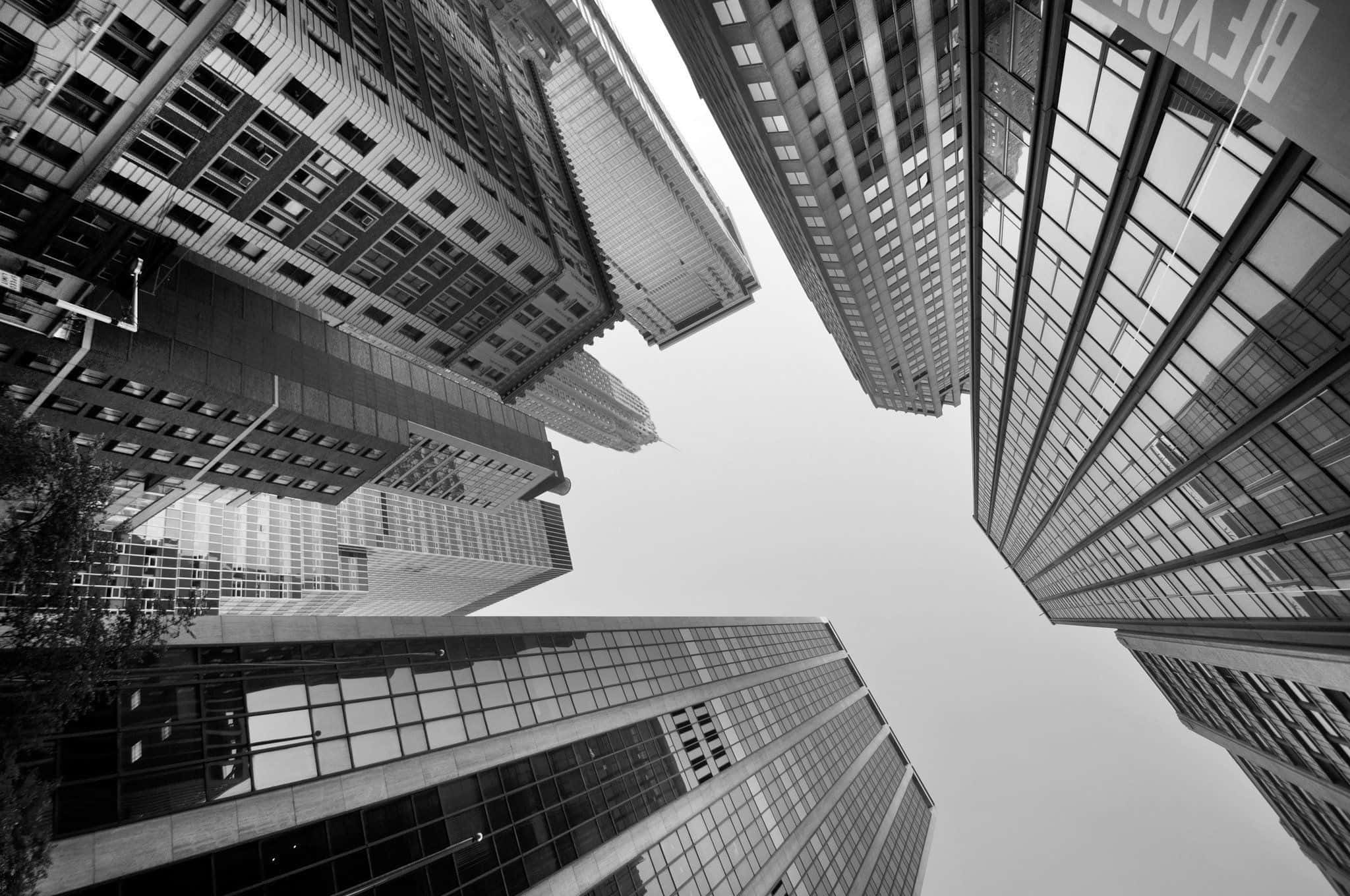 Black And White Architecture 桌布 壁紙 — 一張戲劇性的黑白低角度照片，高聳的玻璃摩天大樓向蒼白的天空匯聚。