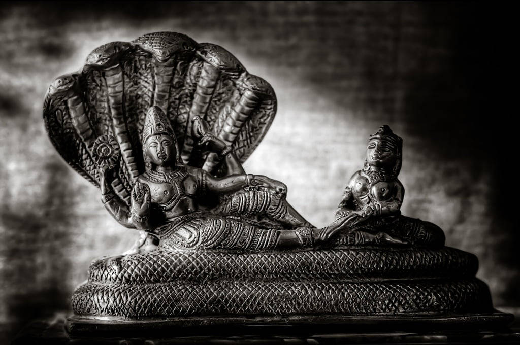 Vishnu 桌布 壁紙 — 一張戲劇性的黑白照片，展示了一尊細節豐富的濕婆神雕像，他斜躺著，身後有眼鏡蛇頭罩，旁邊有一個較小的雕像。