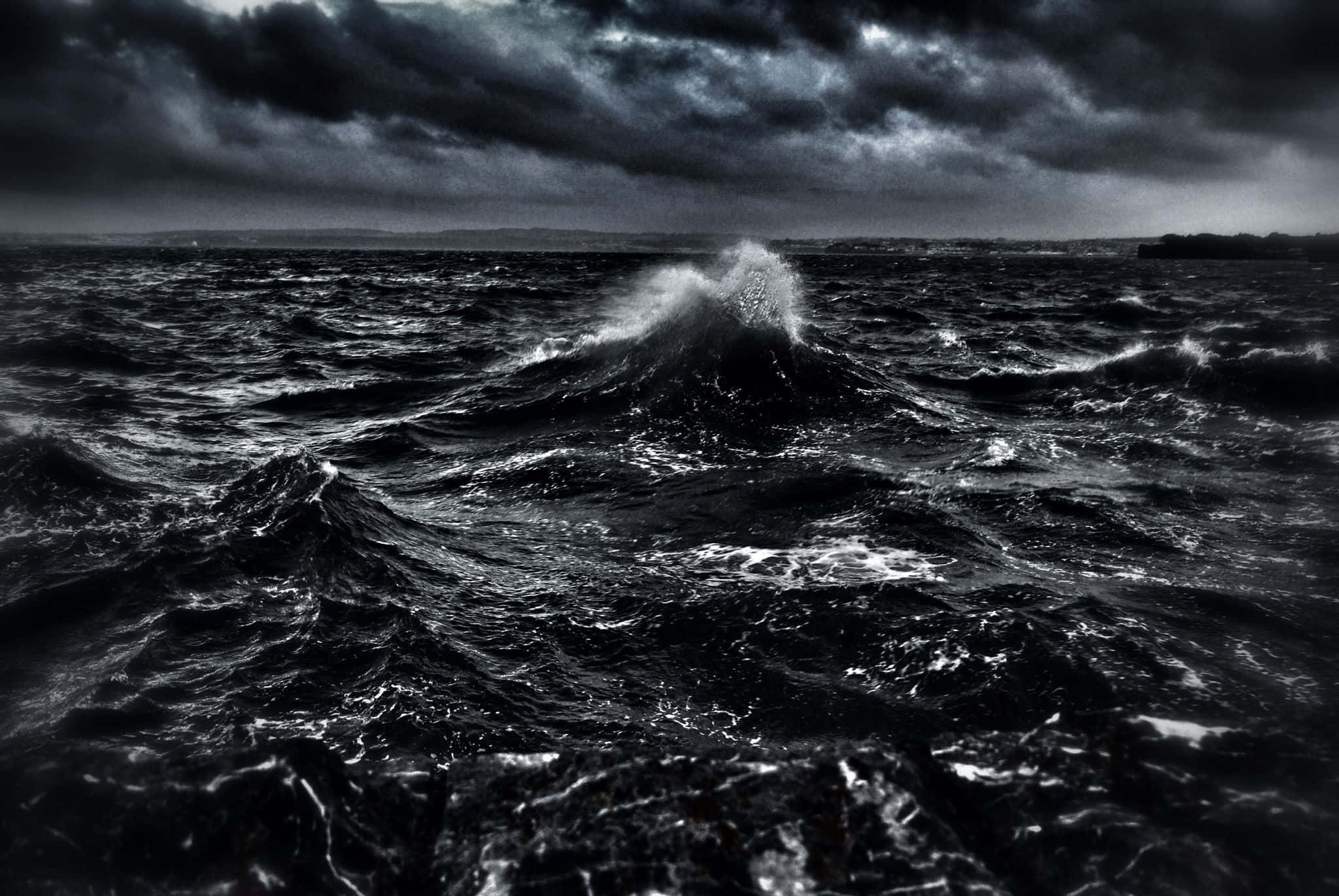 Dark Ocean 桌布 壁紙 — 一張戲劇性的黑白照片，描繪了暴風雨中的大海，巨浪在厚重的雲層下翻騰。