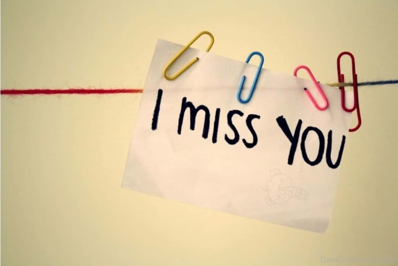 I Miss You 桌布 壁紙 — 一張手寫便條寫著「我想你」，用彩色萬字夾夾在繩子上，背景是柔和的米色牆壁。