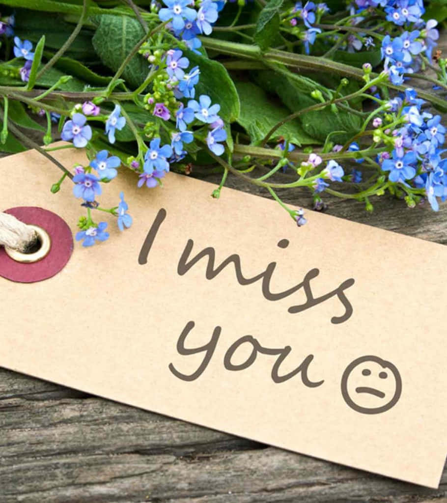 I Miss You 桌布 壁紙 — 一張手寫標籤，上面寫著「我想你」和一個悲傷的表情，旁邊是精緻的藍色勿忘我，放在風化的木頭上。