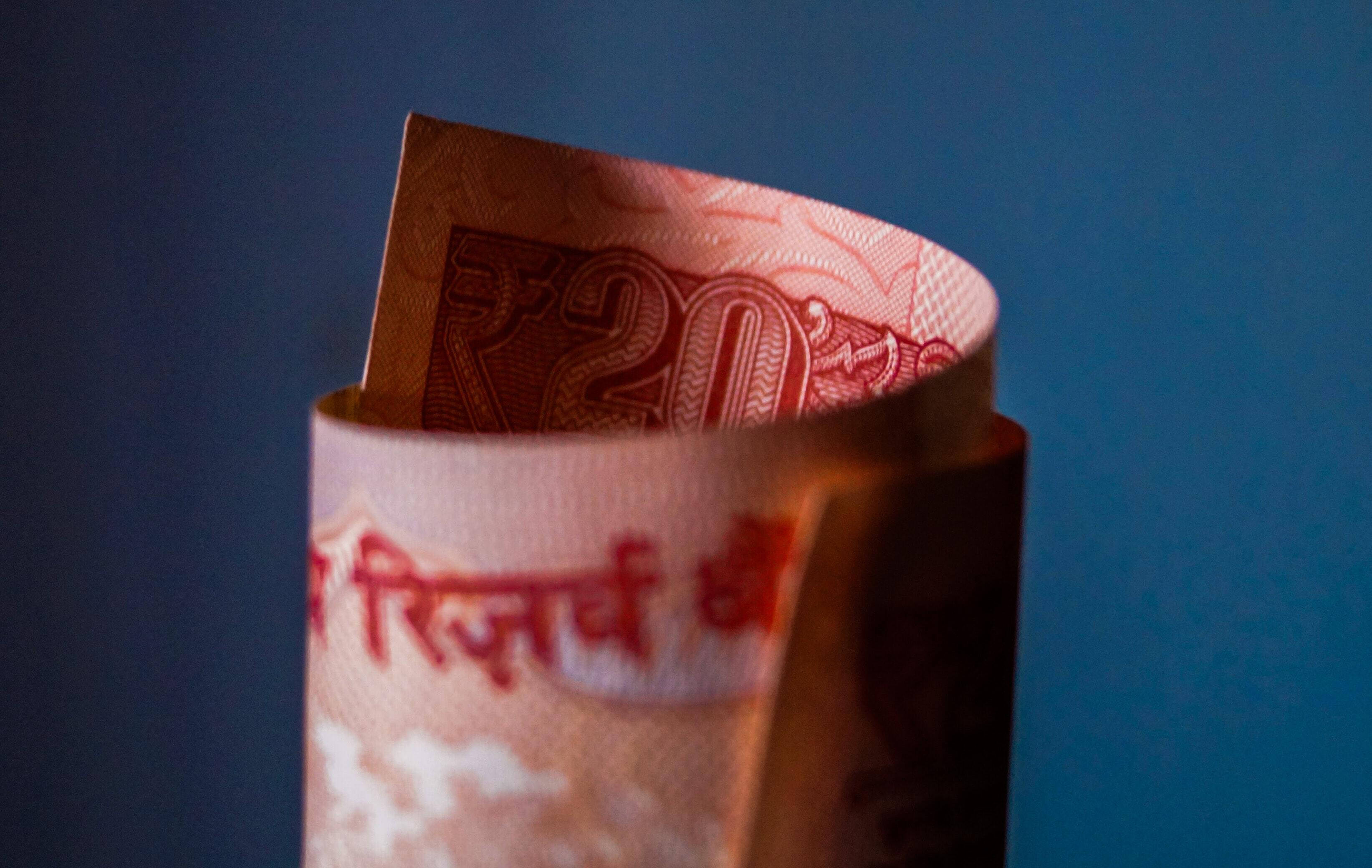 Indian 桌布 壁紙 — 一張捲起的二十盧比印度紙幣在深藍色背景和柔和燈光下直立。