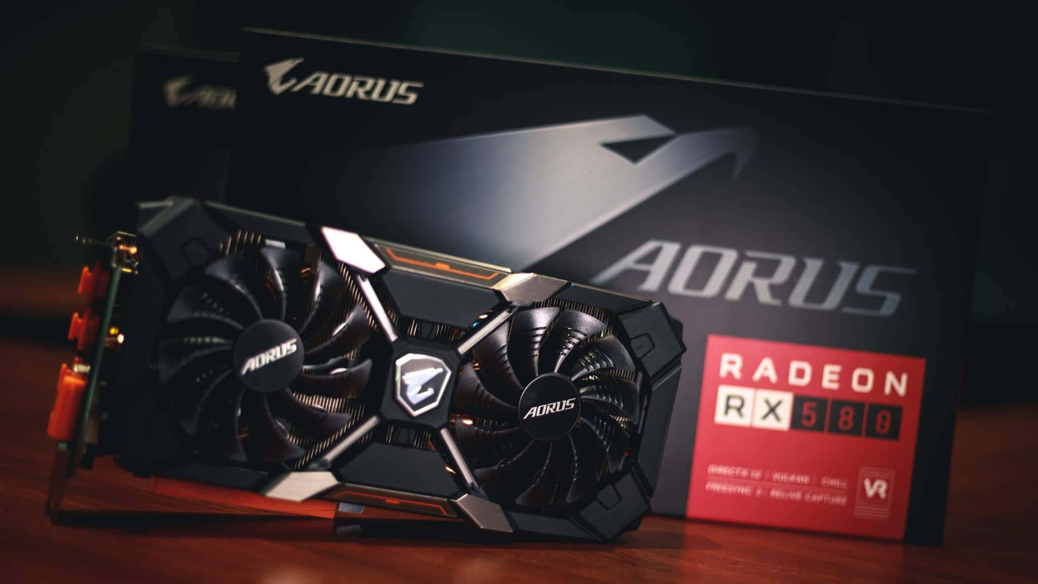 4K Graphics Cards 桌布 壁紙 — 一張時尚黑色Aorus Radeon RX 580顯示卡在戲劇性燈光下放置在木質表面上，旁邊是其品牌包裝盒。