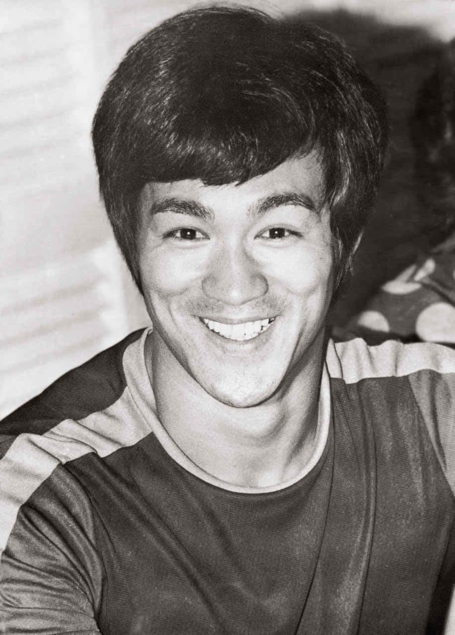 李小龍在黑白照片中微笑，穿著條紋襯衫。