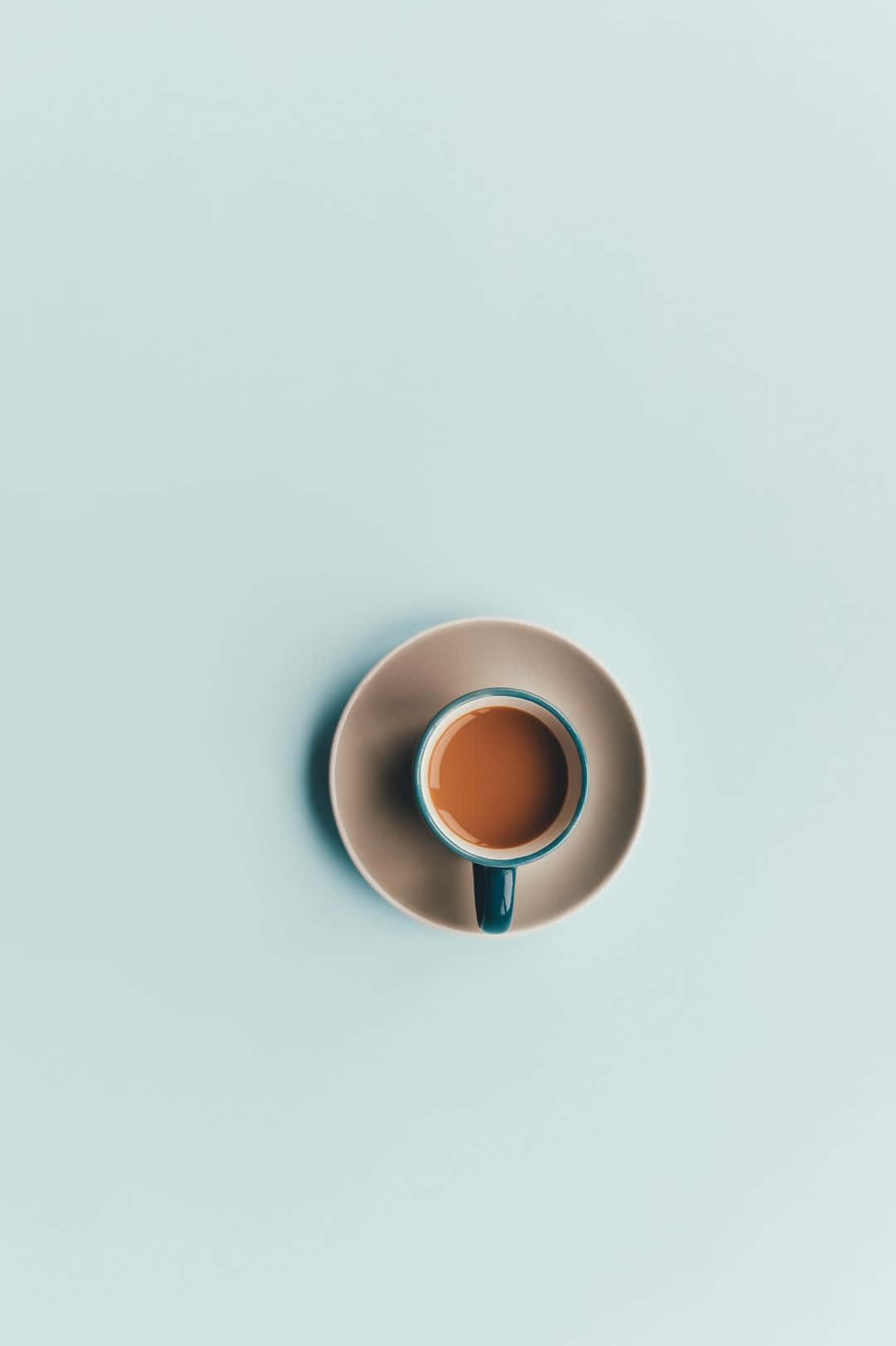 Minimalist Coffee 桌布 壁紙 — 一張極簡風格的俯拍照片，展示一個陶瓷咖啡杯，內有深色液體，放在配套的碟子上，背景是柔和的薄荷綠色。
