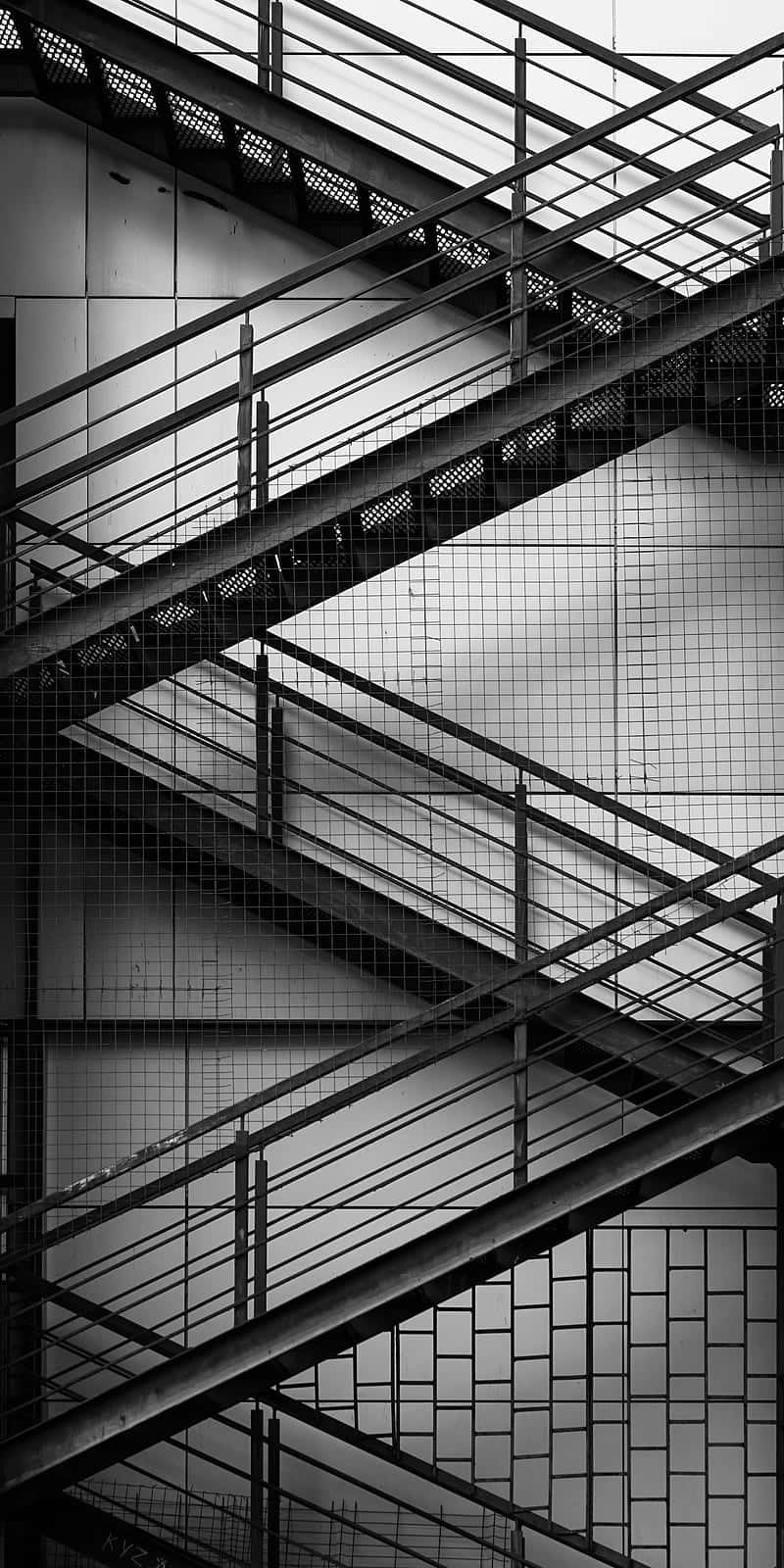 Minimalist Black And White 桌布 壁紙 — 一張清晰的黑白建築照片，展示交錯的金屬樓梯和欄杆，在瓷磚牆上形成幾何圖案。