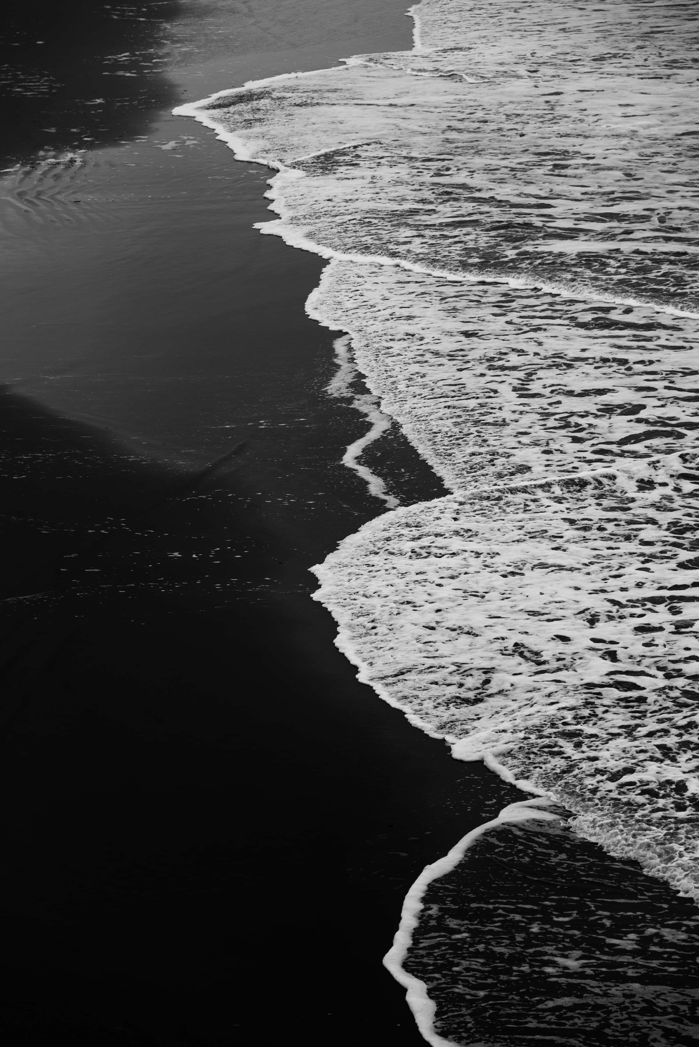 Black And White Beach 桌布 壁紙 — 一張清晰的黑白照片捕捉到泡沫狀的海浪以對角線構圖湧上深色火山沙灘。